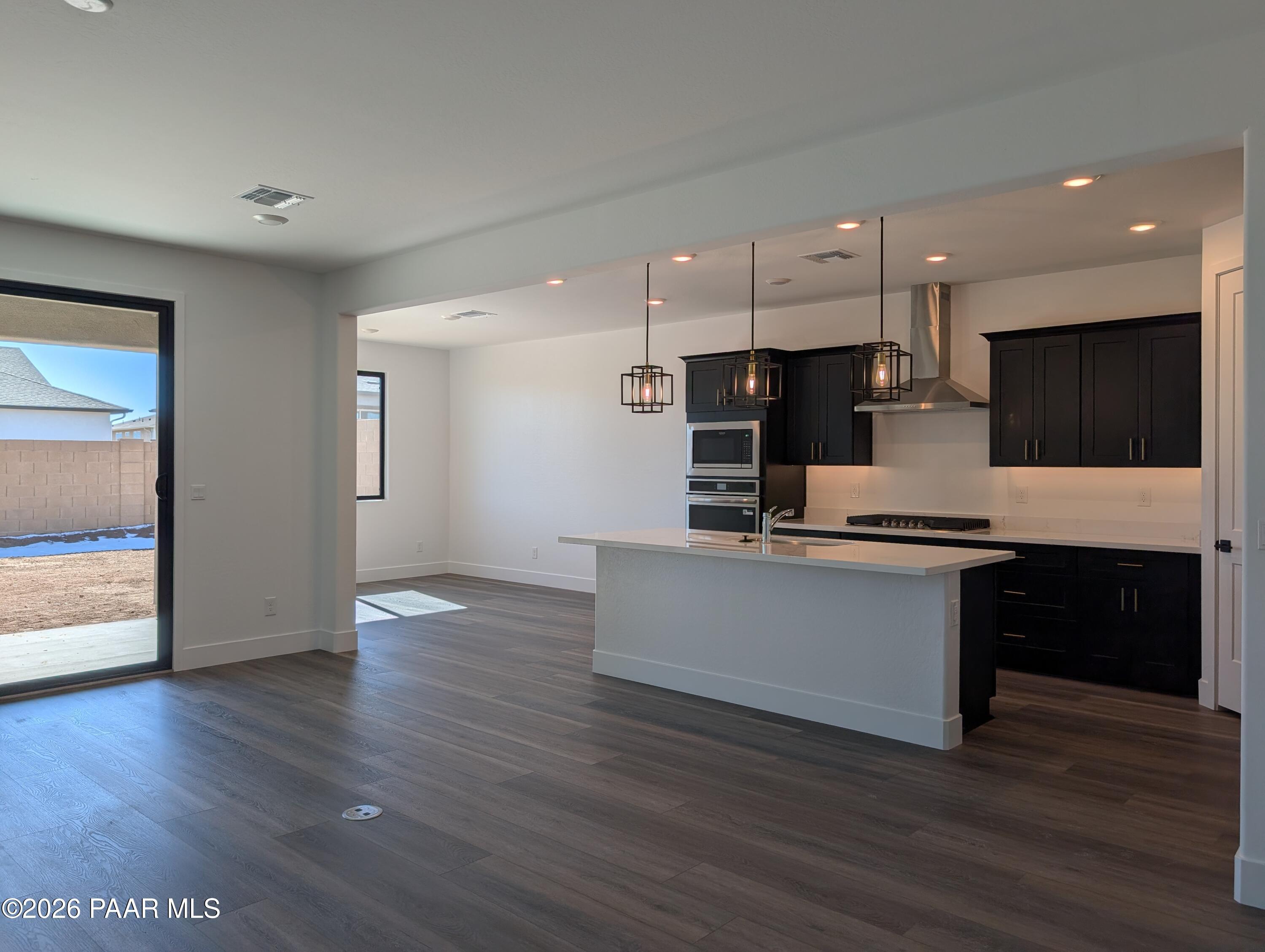 Modern open-concept kitchen with white quartz island, dark cabinets, stainless appliances, and sliding door to backyard in The Sheridan II G, Prescott, AZ