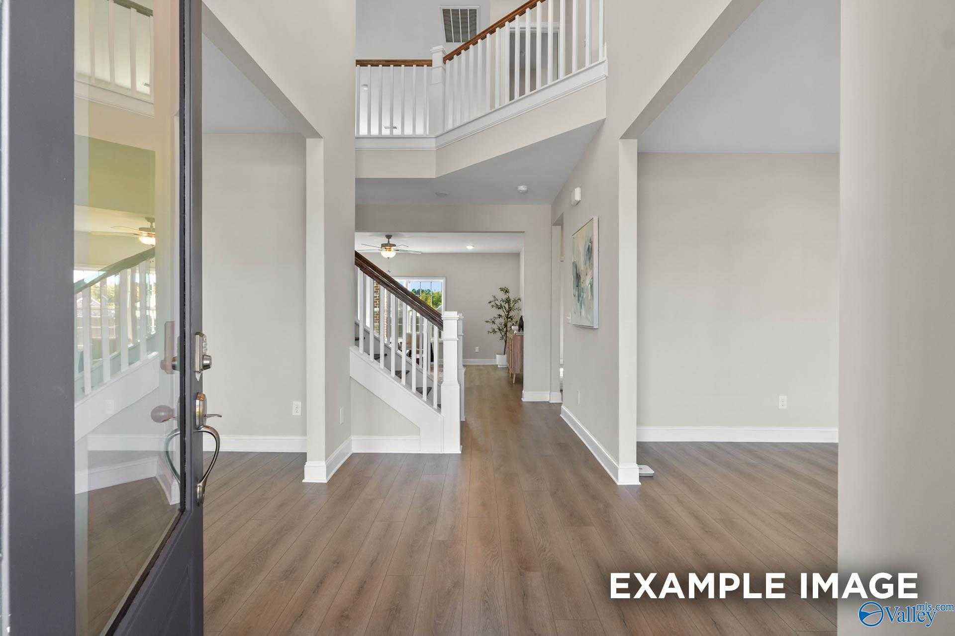 Grand two-story foyer with sweeping wooden staircase, hardwood floors, and neutral walls in Davidson Homes Madison A, Harvest AL