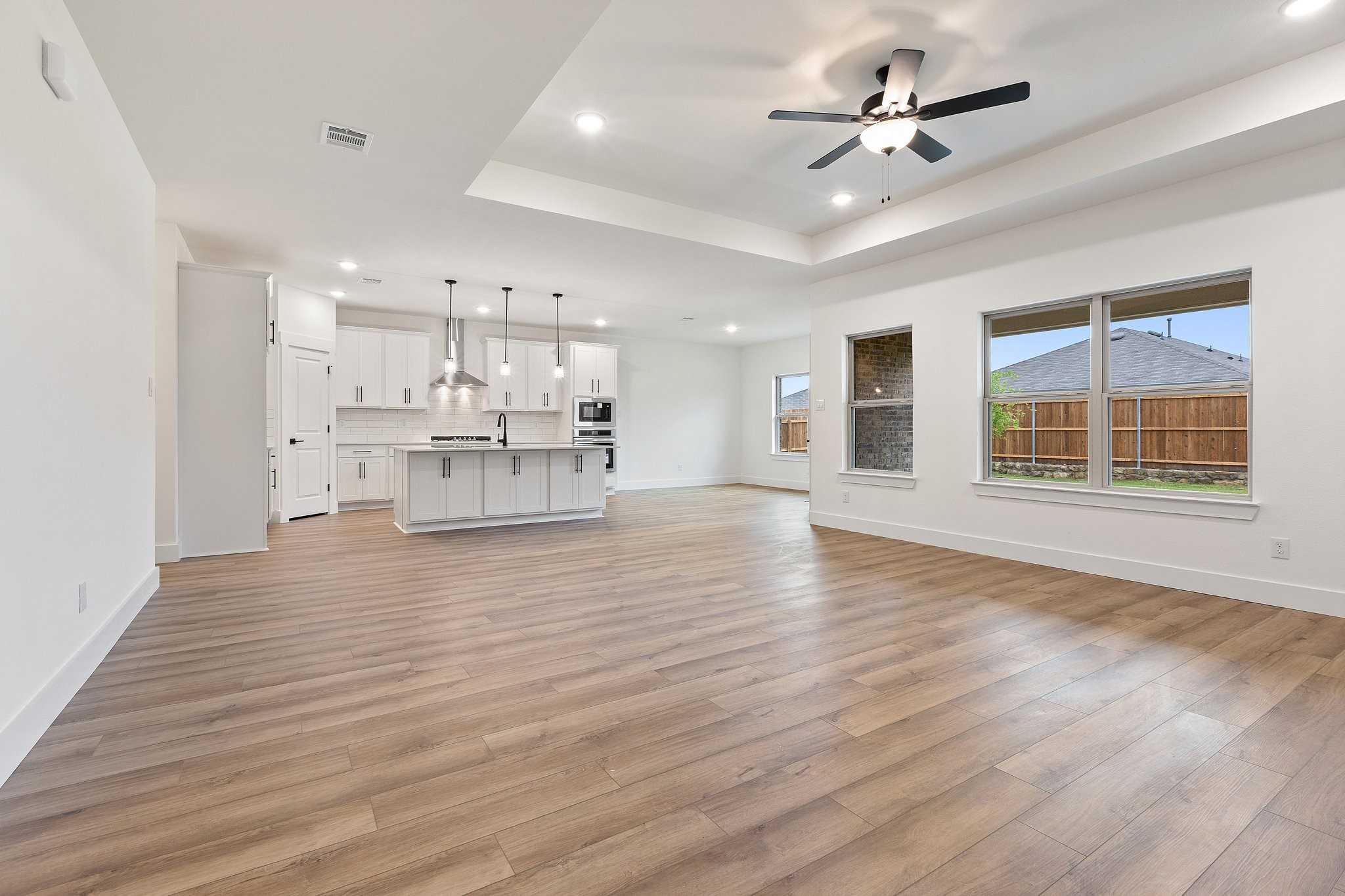 Open-concept living and kitchen with white shaker cabinets, large island, ceiling fans, and backyard views in Davidson Homes The Rockford C, Josephine, Texas