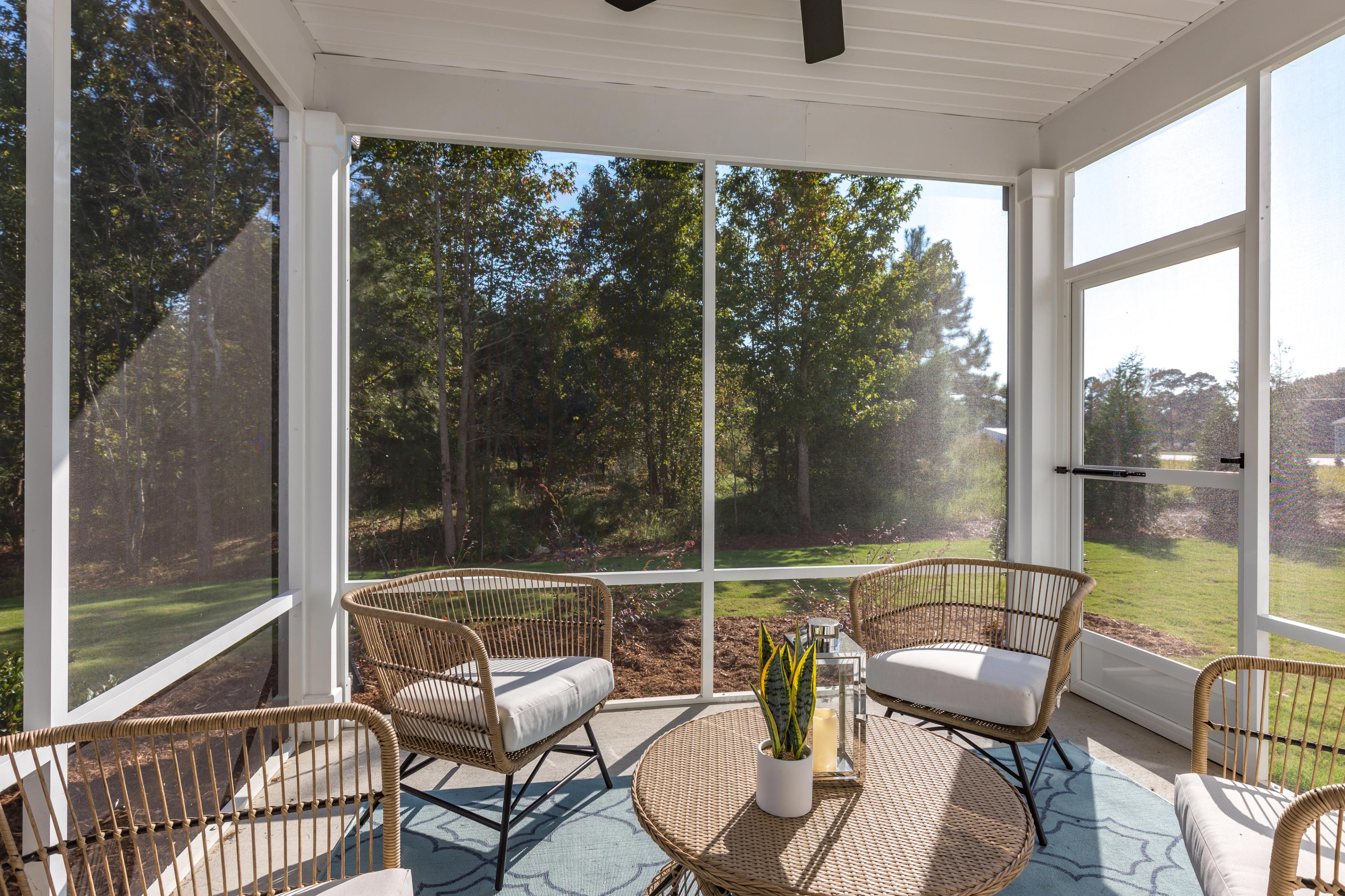 Screened porch with rattan chairs, coffee table, plants and ceiling fan at Enclave at Belmont in Belmont NC overlooking wooded yard