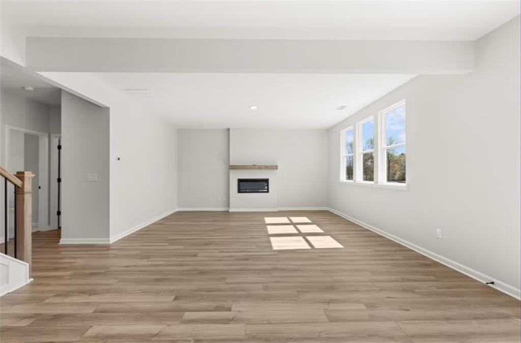 Spacious living room featuring gas fireplace, hardwood floors, large windows, and staircase in The Hickory B by Davidson Homes, Winder, GA
