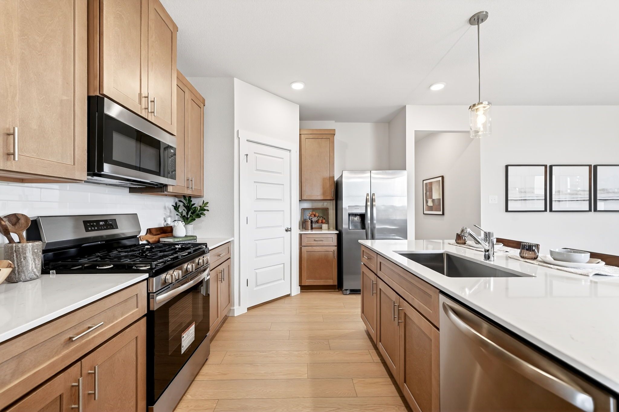 Modern kitchen in Heartland Texas by Davidson Homes featuring oak shaker cabinets, white quartz counters, stainless steel appliances, hardwood floors