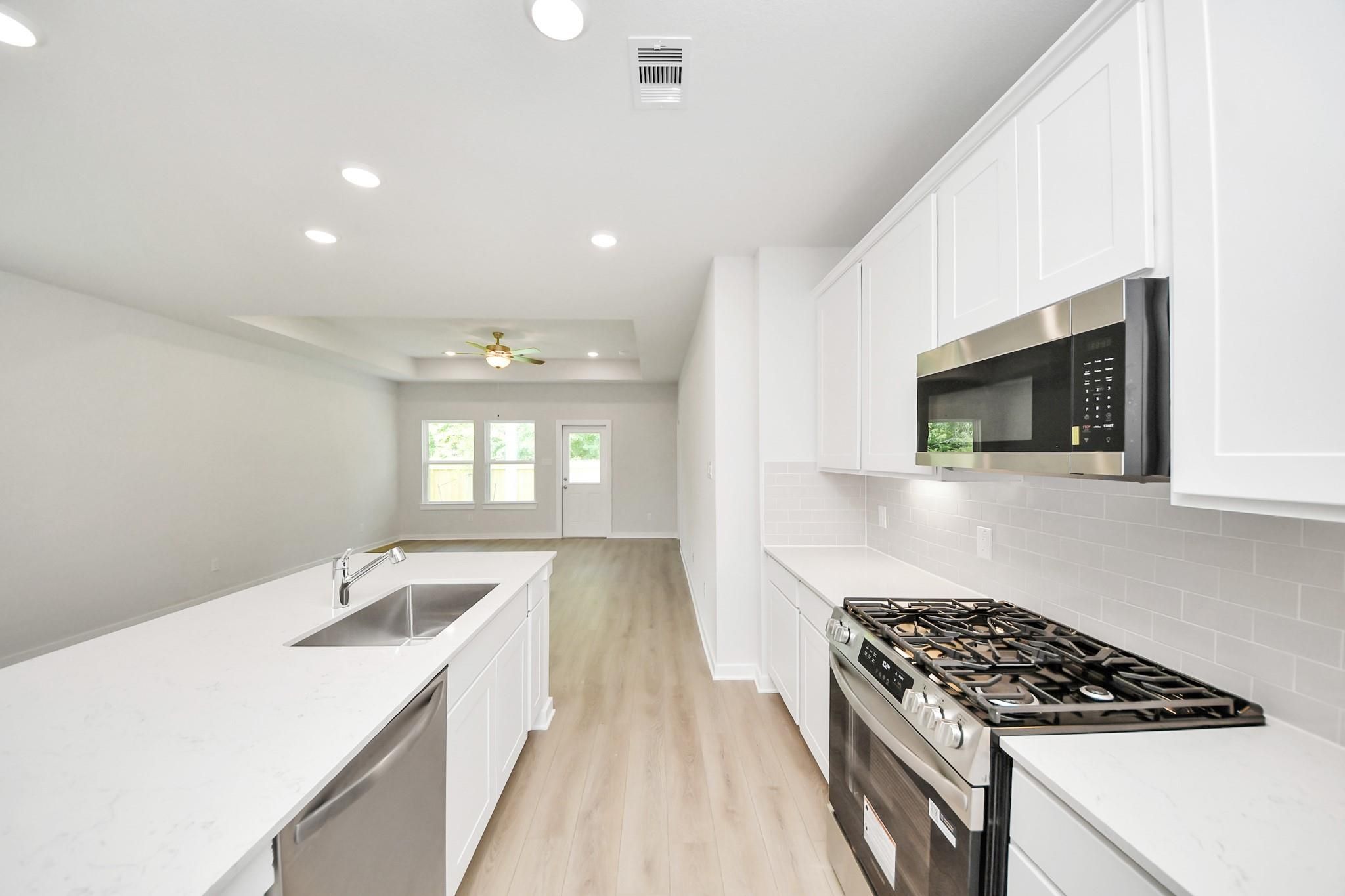 Modern kitchen with white cabinets, quartz countertops, and stainless appliances in The Blanco E floor plan, Conroe, Texas.