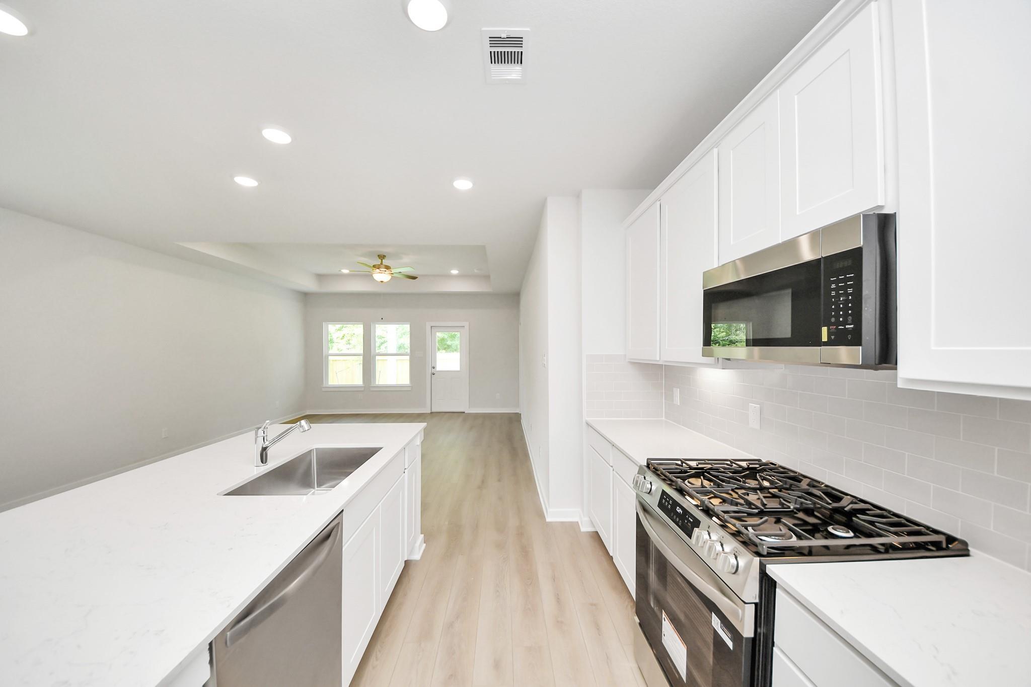 Modern kitchen with white cabinets, quartz countertops, and stainless appliances in The Blanco E floor plan, Conroe, Texas.