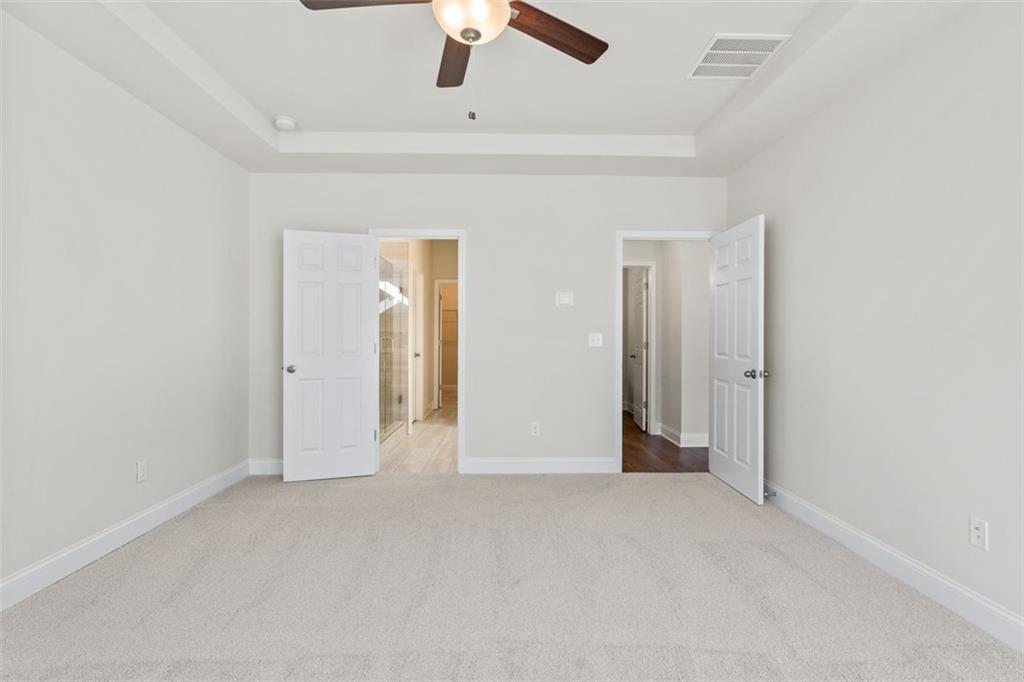 Empty bedroom with open closet and bathroom doors, ceiling fan in Davidson Homes The Ash C at Wehunt Meadows, Hoschton, GA