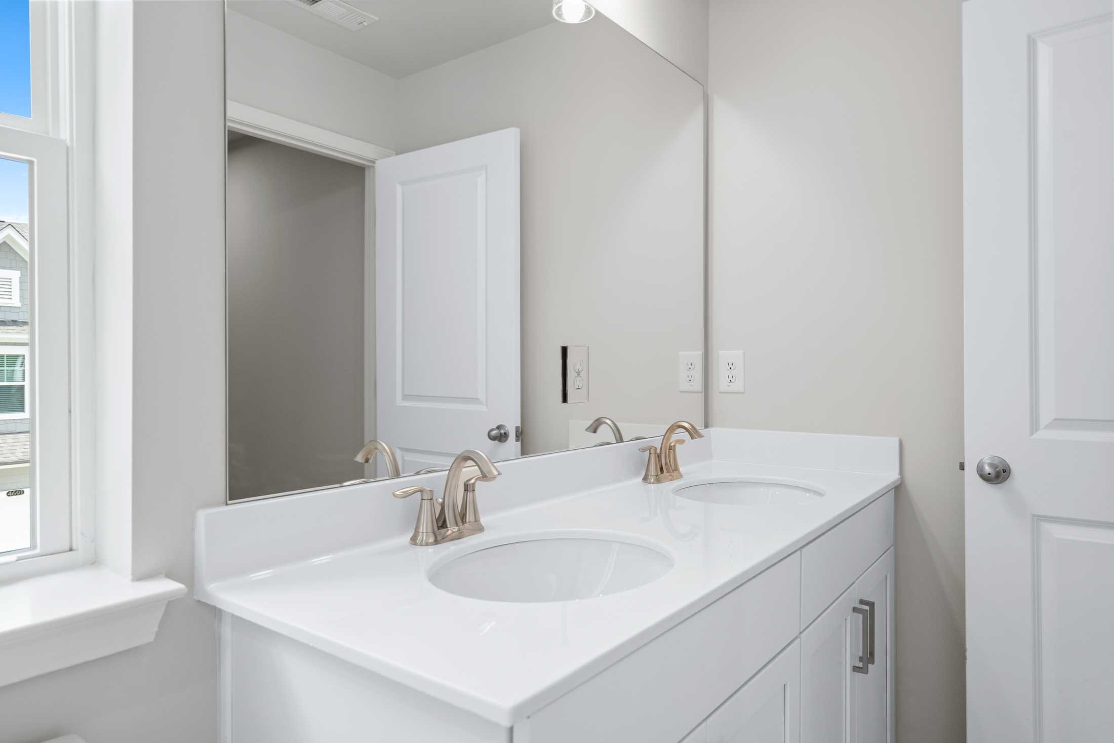 Spacious master bathroom vanity in The Cary A featuring double white sinks, gold faucets, and frameless mirrors