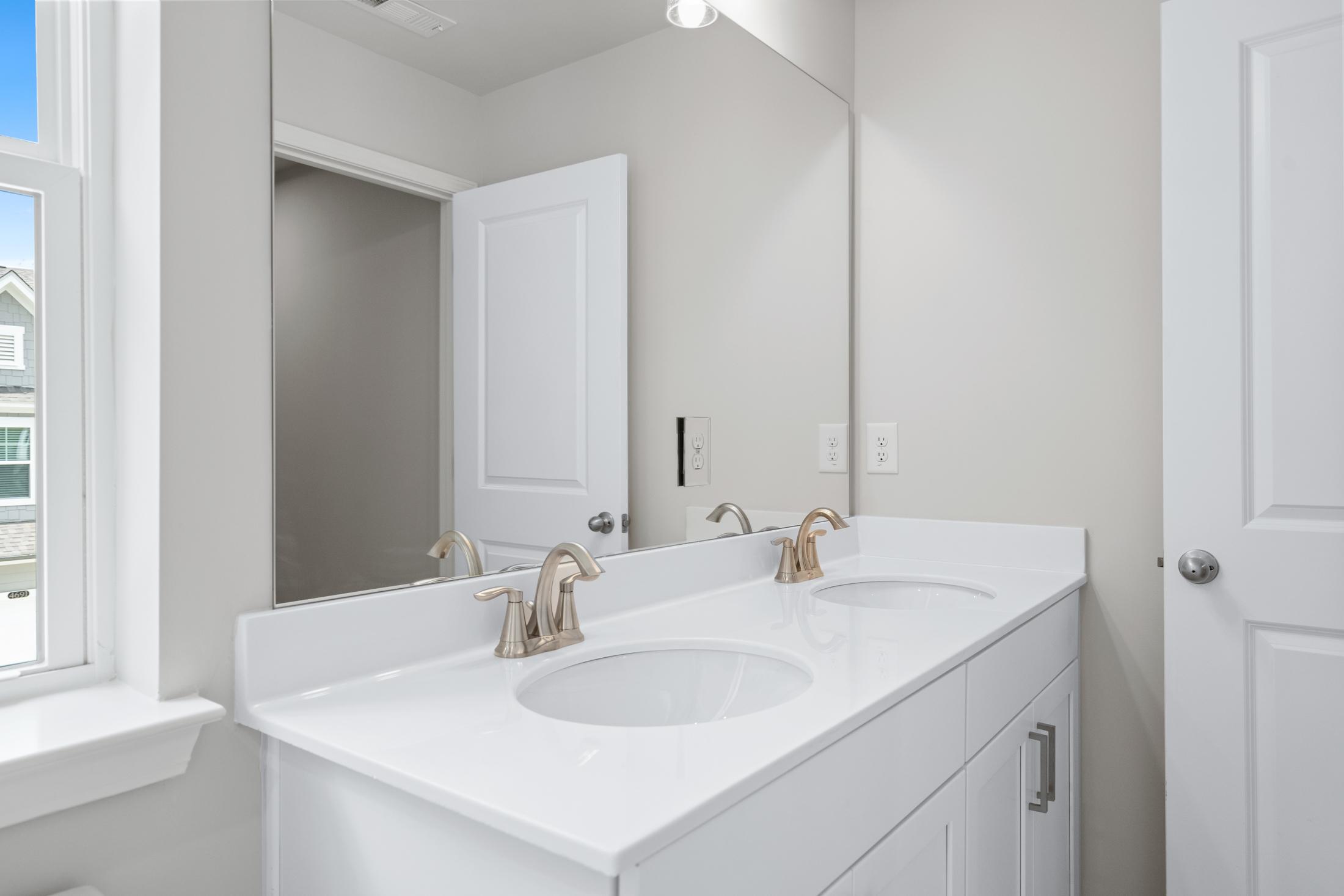 Spacious master bathroom vanity in The Cary A featuring double white sinks, gold faucets, and frameless mirrors