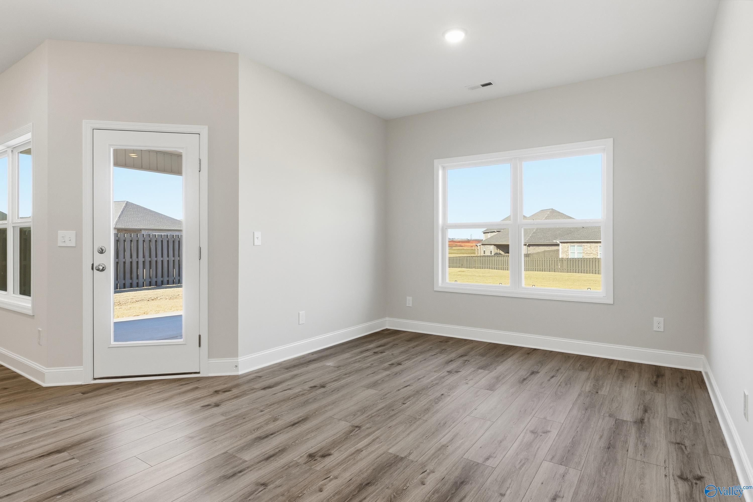 Bright living room with hardwood floors, large windows, and glass door to backyard in The Everett home, Creekside, Harvest AL
