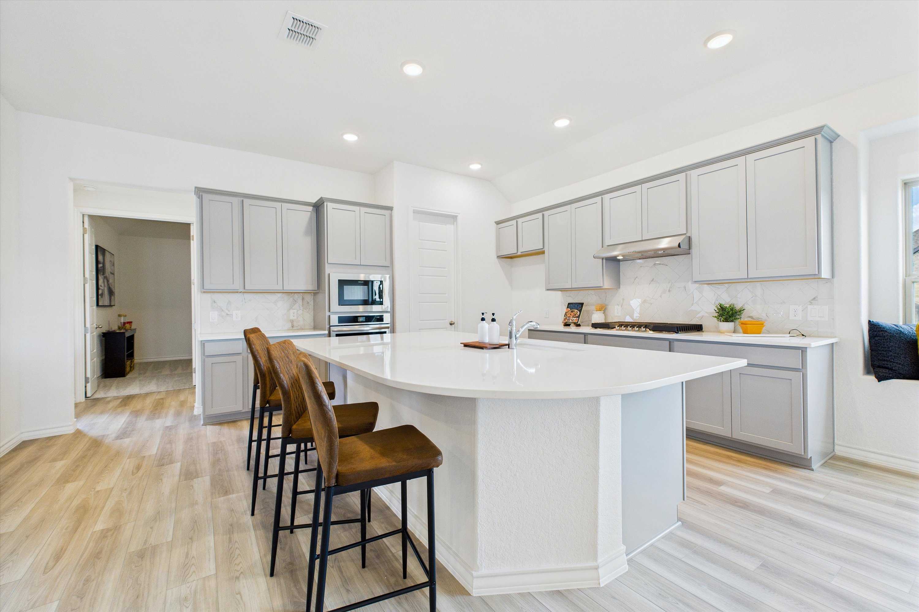 Modern kitchen with gray shaker cabinets, white quartz island, stainless appliances, and bar stools in Davidson Homes Summerlin C, Castroville, TX