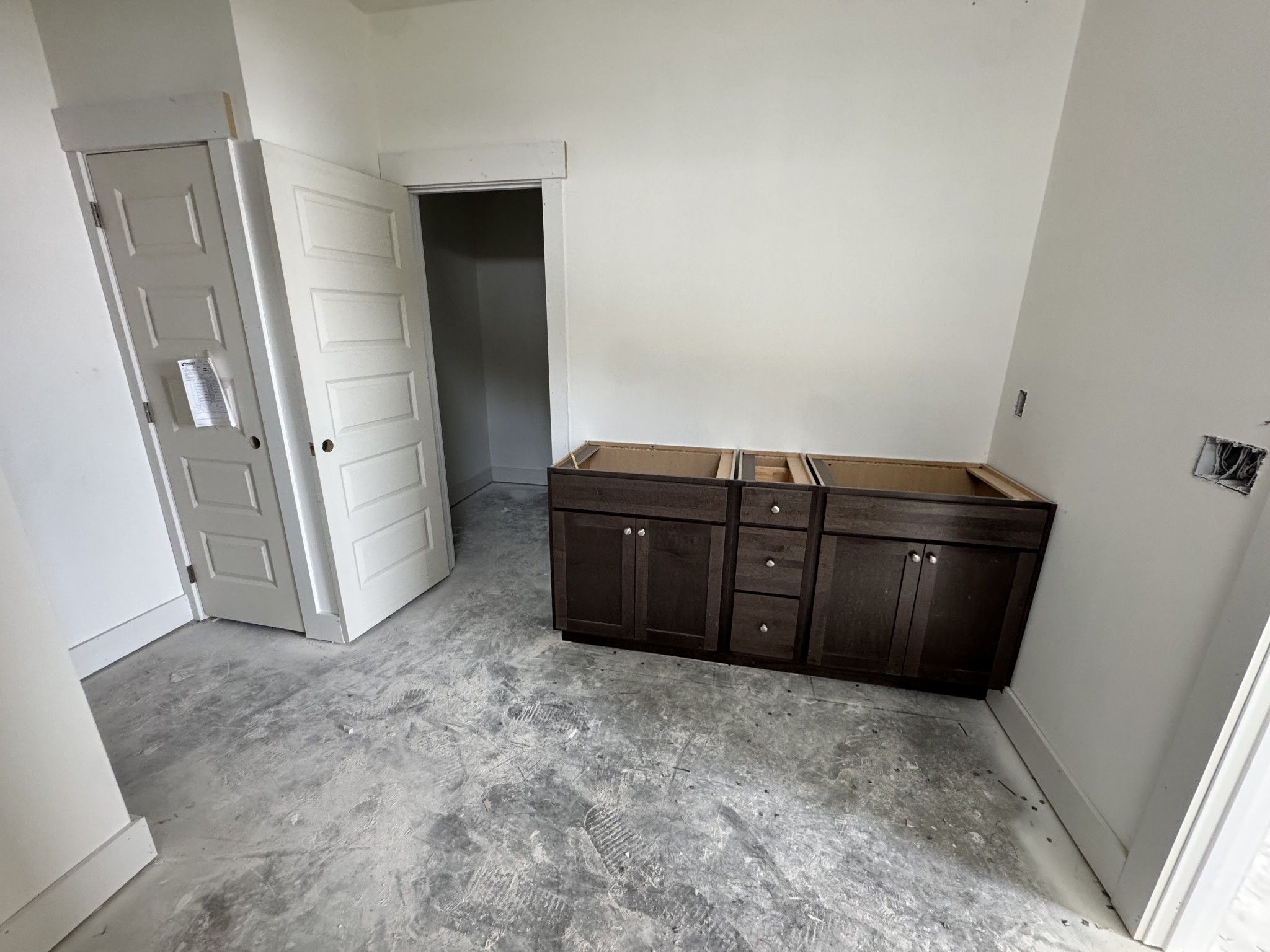 Unfinished kitchen with dark wood base cabinets, open doorways, white walls in The Cottonwood E by Davidson Homes, Gallatin, TN