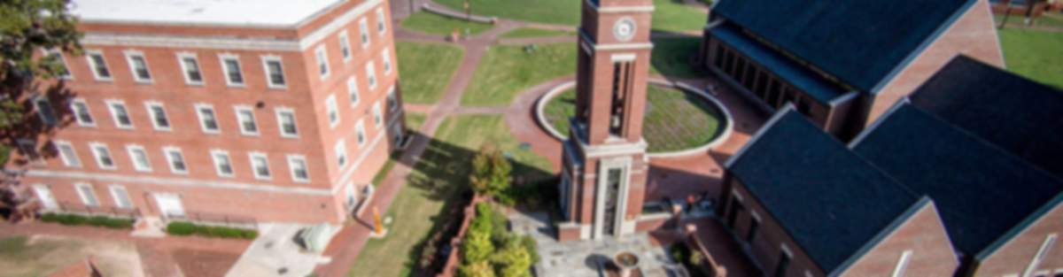 Aerial view of Buies Creek campus with red brick buildings, clock tower, and lush green lawns near new home communities