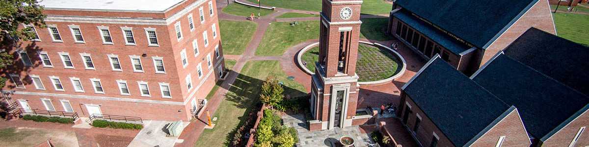 Aerial view of Buies Creek campus with red brick buildings, clock tower, and lush green lawns near new home communities