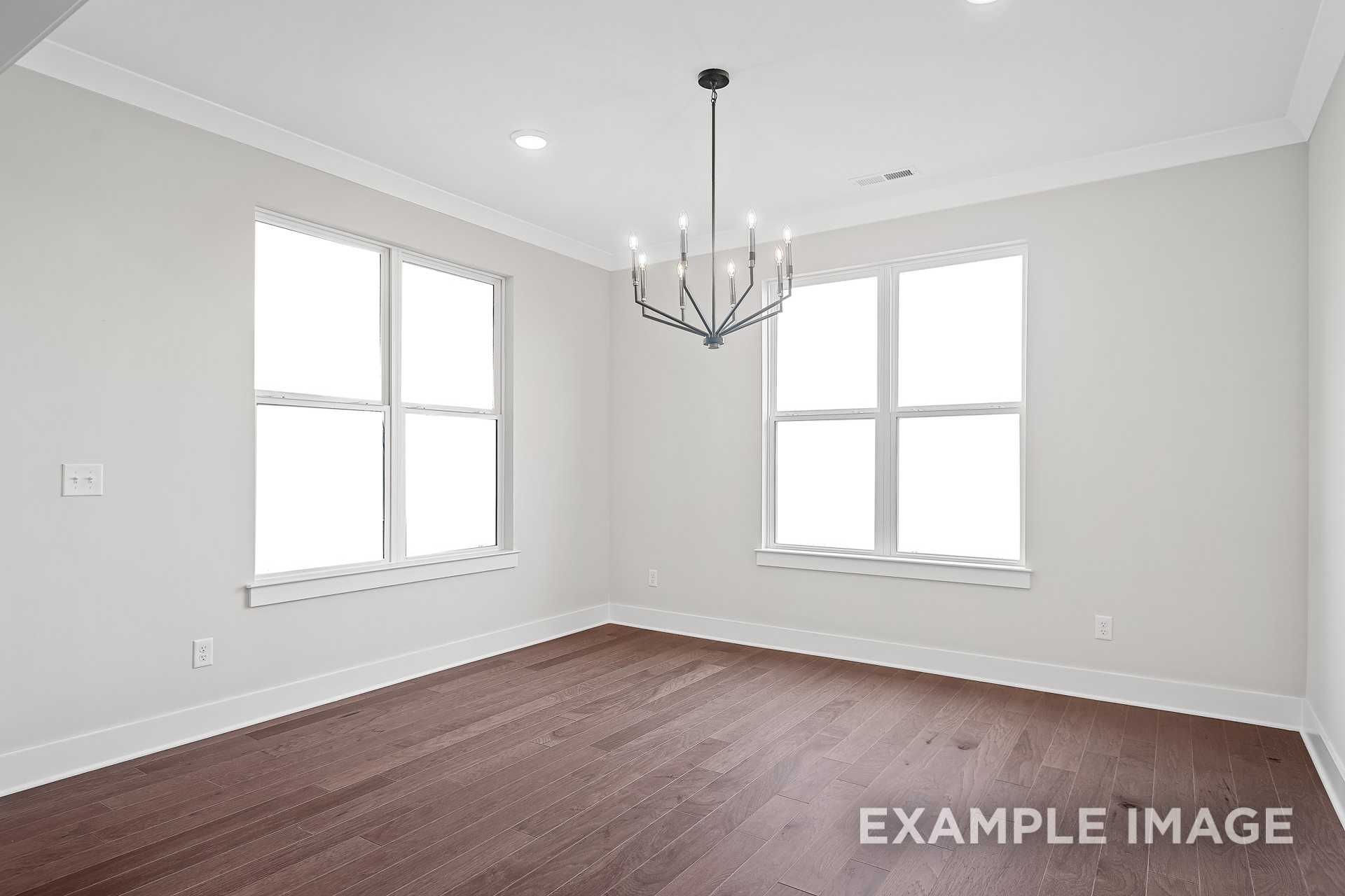 Bright dining room in The Hathaway home design with light gray walls, dark hardwood floors, large windows, and modern black chandelier