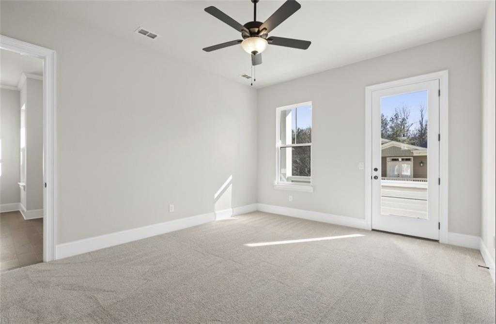 Spacious bedroom featuring light gray walls, beige carpet, ceiling fan, large windows, and French door to backyard in Davidson Homes Seaside A, Woodstock, GA