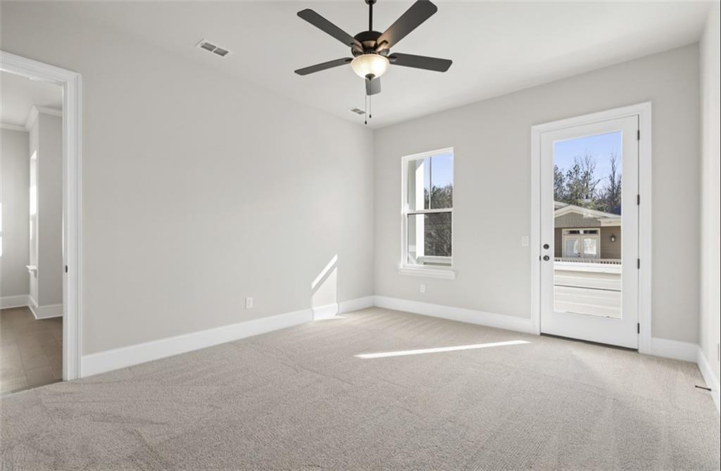 Spacious bedroom featuring light gray walls, beige carpet, ceiling fan, large windows, and French door to backyard in Davidson Homes Seaside A, Woodstock, GA