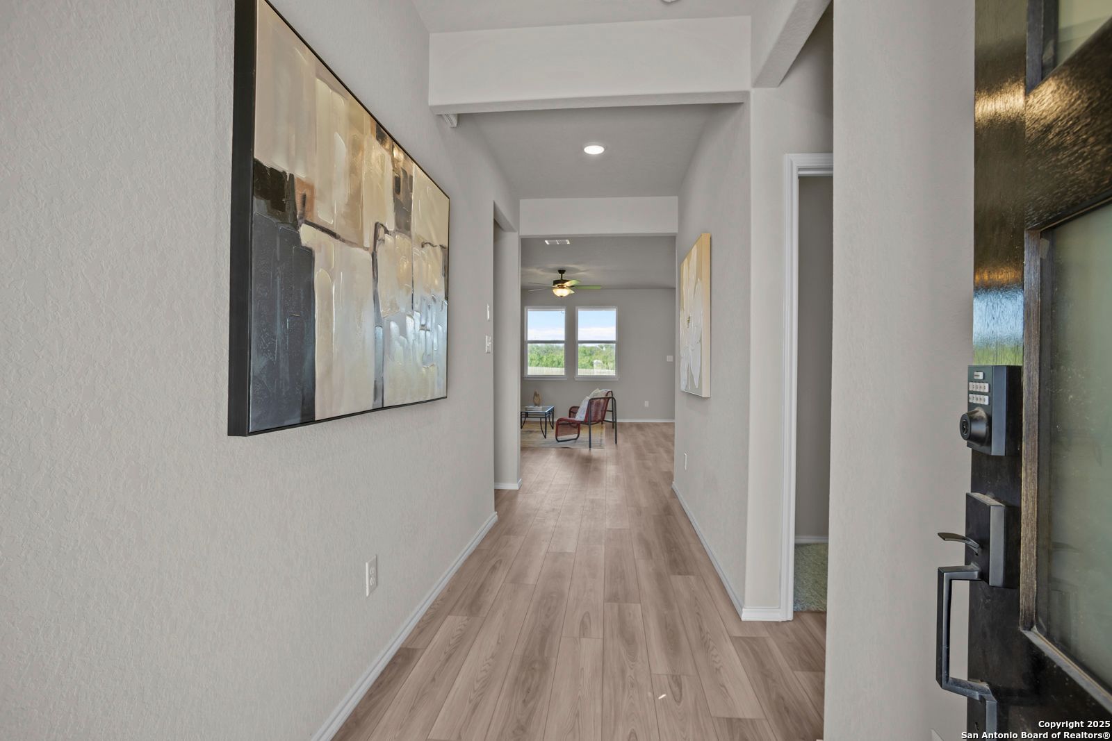 Elegant hallway with light hardwood floors, abstract wall art, and sunlit windows in Davidson Homes The Asheville H, Converse, Texas
