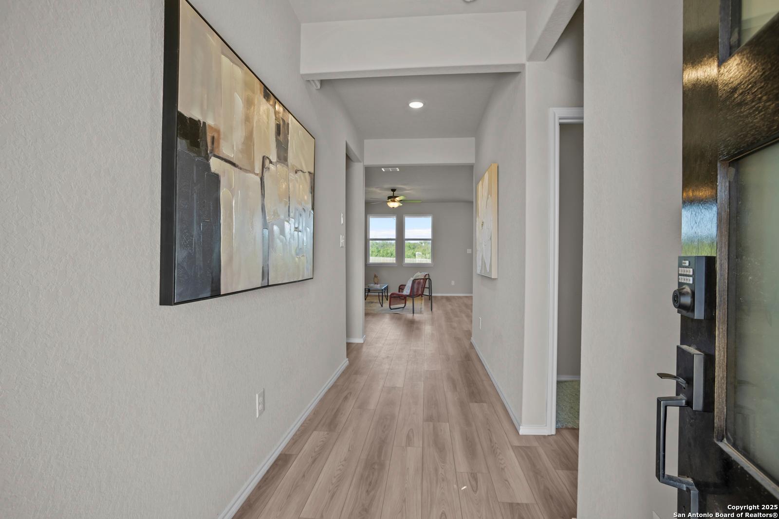 Elegant hallway with light hardwood floors, abstract wall art, and sunlit windows in Davidson Homes The Asheville H, Converse, Texas
