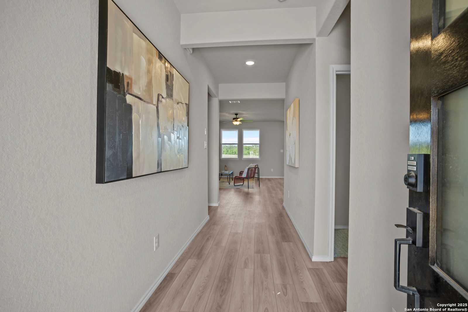 Elegant hallway with light hardwood floors, abstract wall art, and sunlit windows in Davidson Homes The Asheville H, Converse, Texas