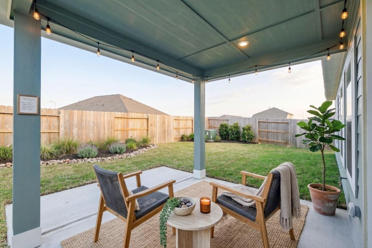 Cozy covered back patio with string lights, lounge chairs, plants, and lush backyard in Davidson Homes The Luna J, Sunterra, Katy