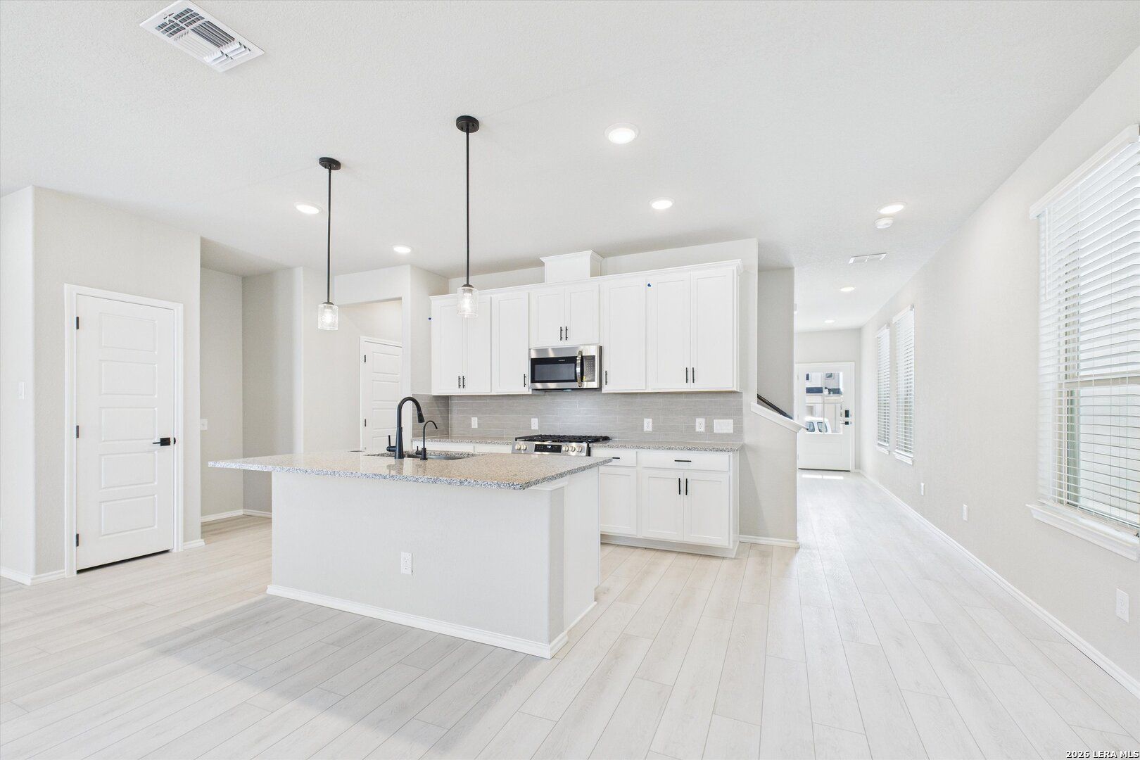 Bright open-concept kitchen with white cabinets, granite island, stainless appliances in Davidson Homes The Charlotte A, San Antonio