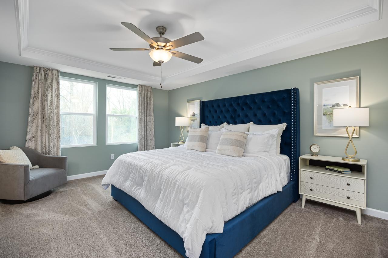 Spacious primary bedroom at Gregory Village Townhomes in Lillington NC with navy velvet headboard, white bedding, and ceiling fan