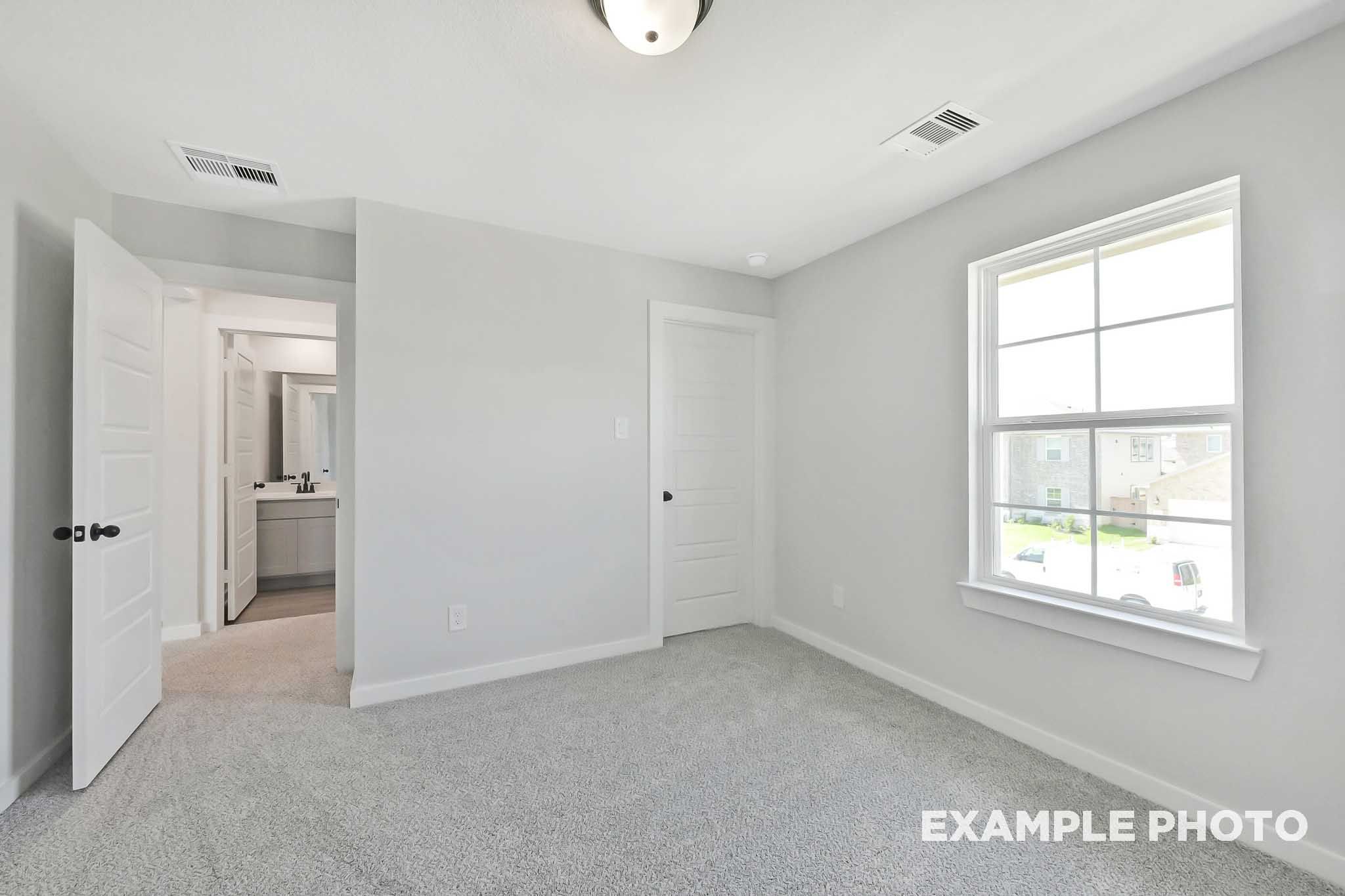 Spacious bedroom in The Sequoia home design with attached bath, gray walls, carpet flooring, and large window