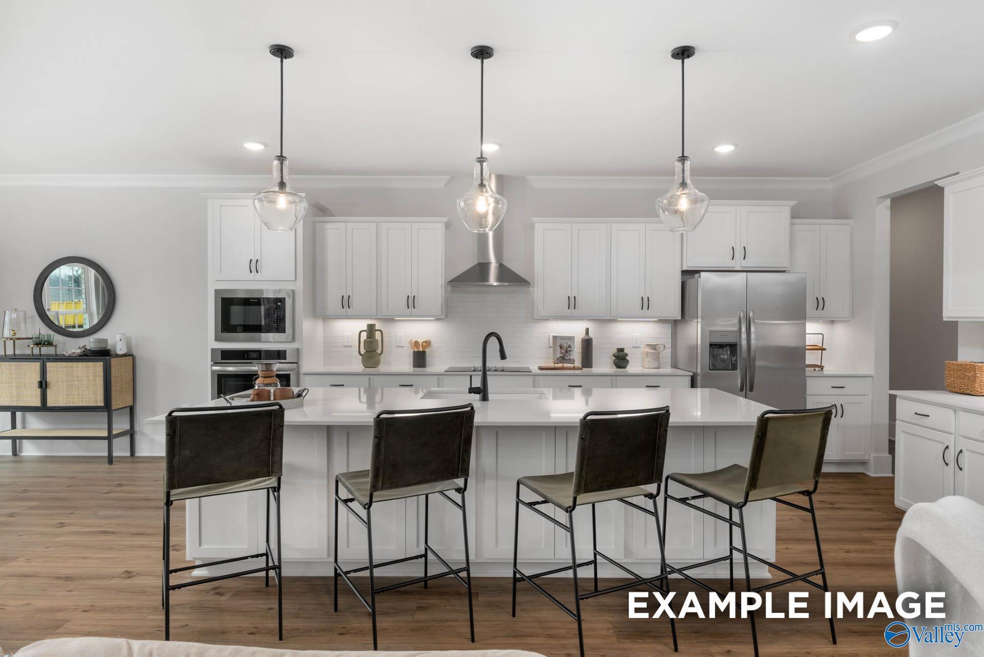 Modern white open-concept kitchen with island, bar stools, stainless appliances, and pendant lights in The Finleigh by Davidson Homes, Decatur AL