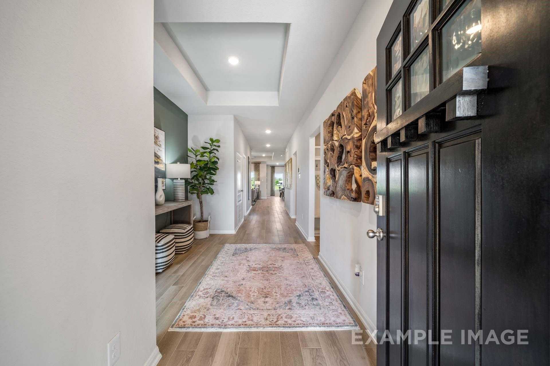 Elegant hallway with tray ceiling, hardwood floors, Persian rug, and wall art in Davidson Homes The Acadia A, Lago Mar, Texas City