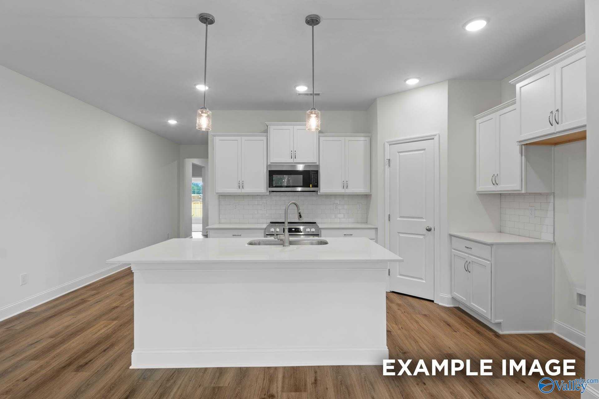 Modern white kitchen island with sink, stainless steel appliances, and pendant lights in Davidson Homes The Daphne D, Athens AL