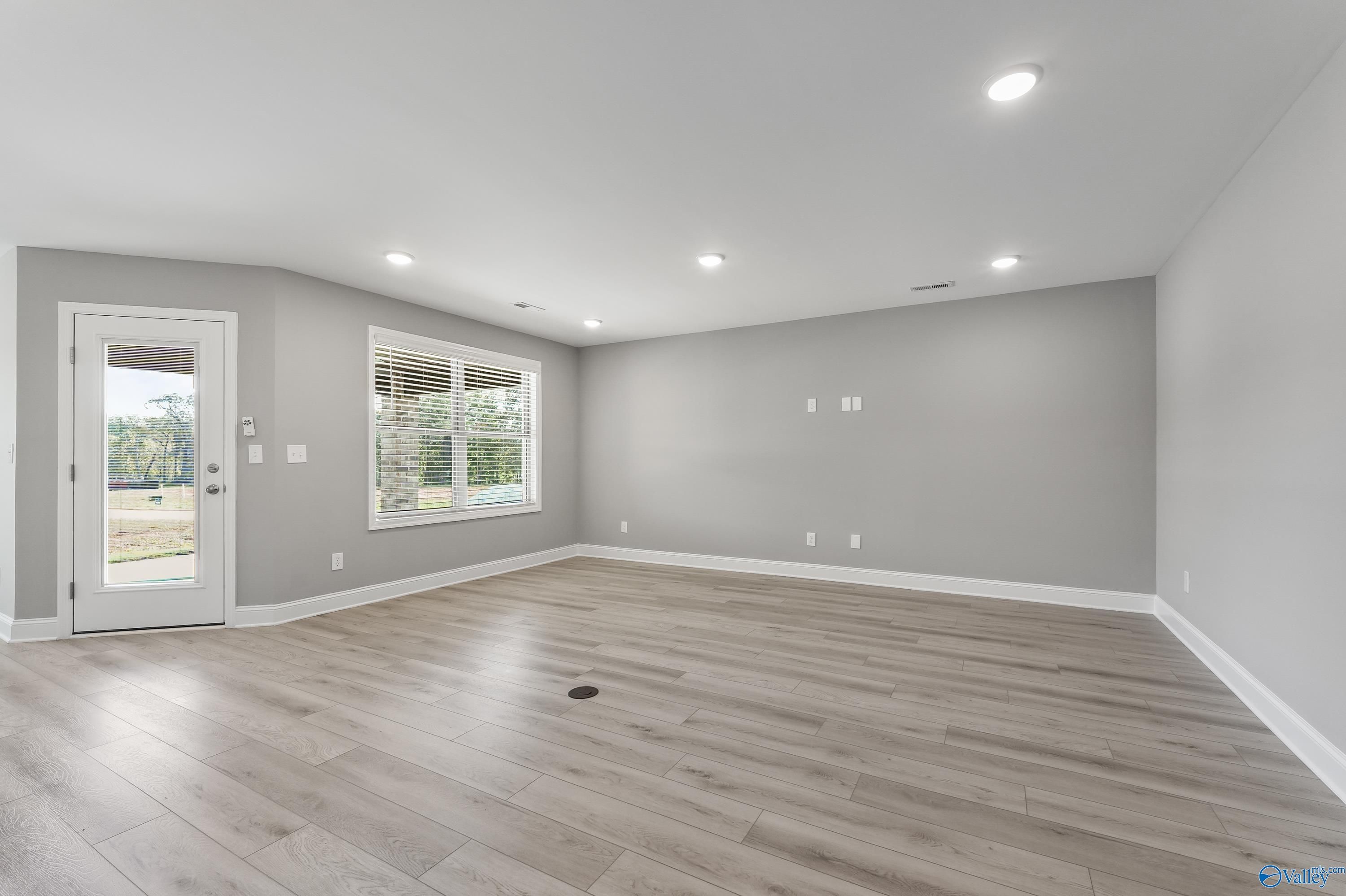 Spacious empty living room with gray walls, light wood floors, and sliding door to backyard in The Everett B home, Athens, Alabama