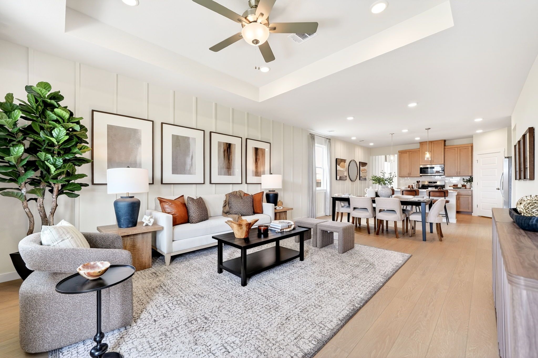 Open-concept living room at Heartland Texas by Davidson Homes with white shiplap walls, fiddle leaf plant, white sofa, and adjacent kitchen