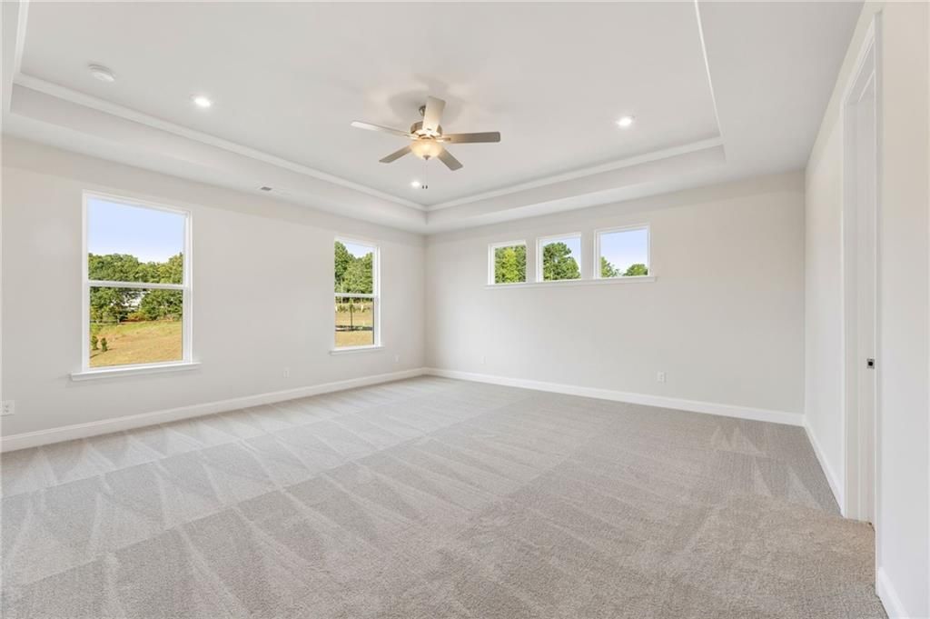 Bright upstairs bedroom with large windows overlooking trees and fields, ceiling fan, and gray carpet in Davidson Homes The Hampton C, Buford, GA