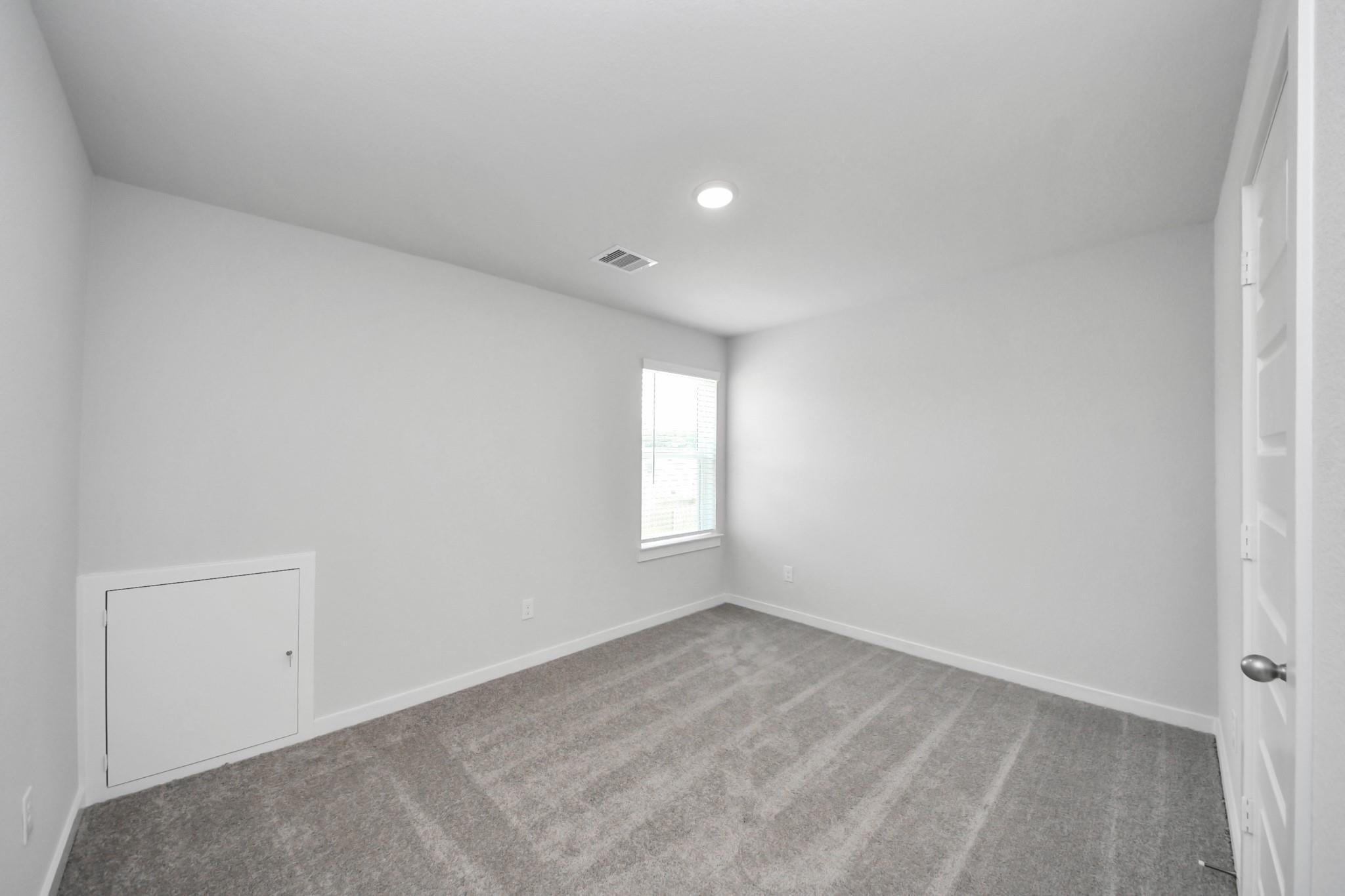 Spacious bedroom with grey carpet and under-eave storage in The Brazos F floor plan, Liberty Estates, Cleveland, Texas.