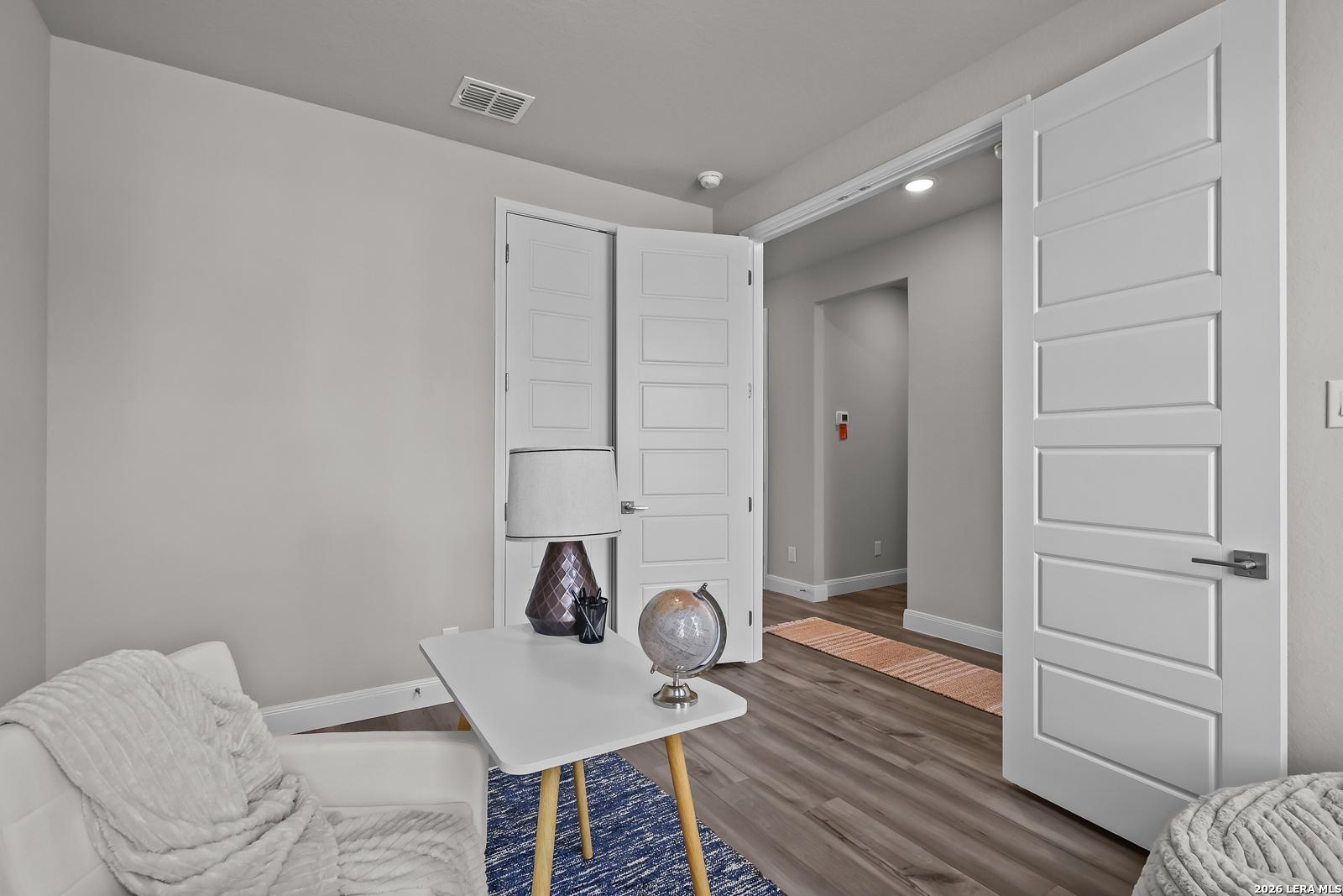 Cozy entryway featuring white double doors, small table with lamp and globe, armchair on wood floors in The Rockford G by Davidson Homes, Ladera, San Antonio