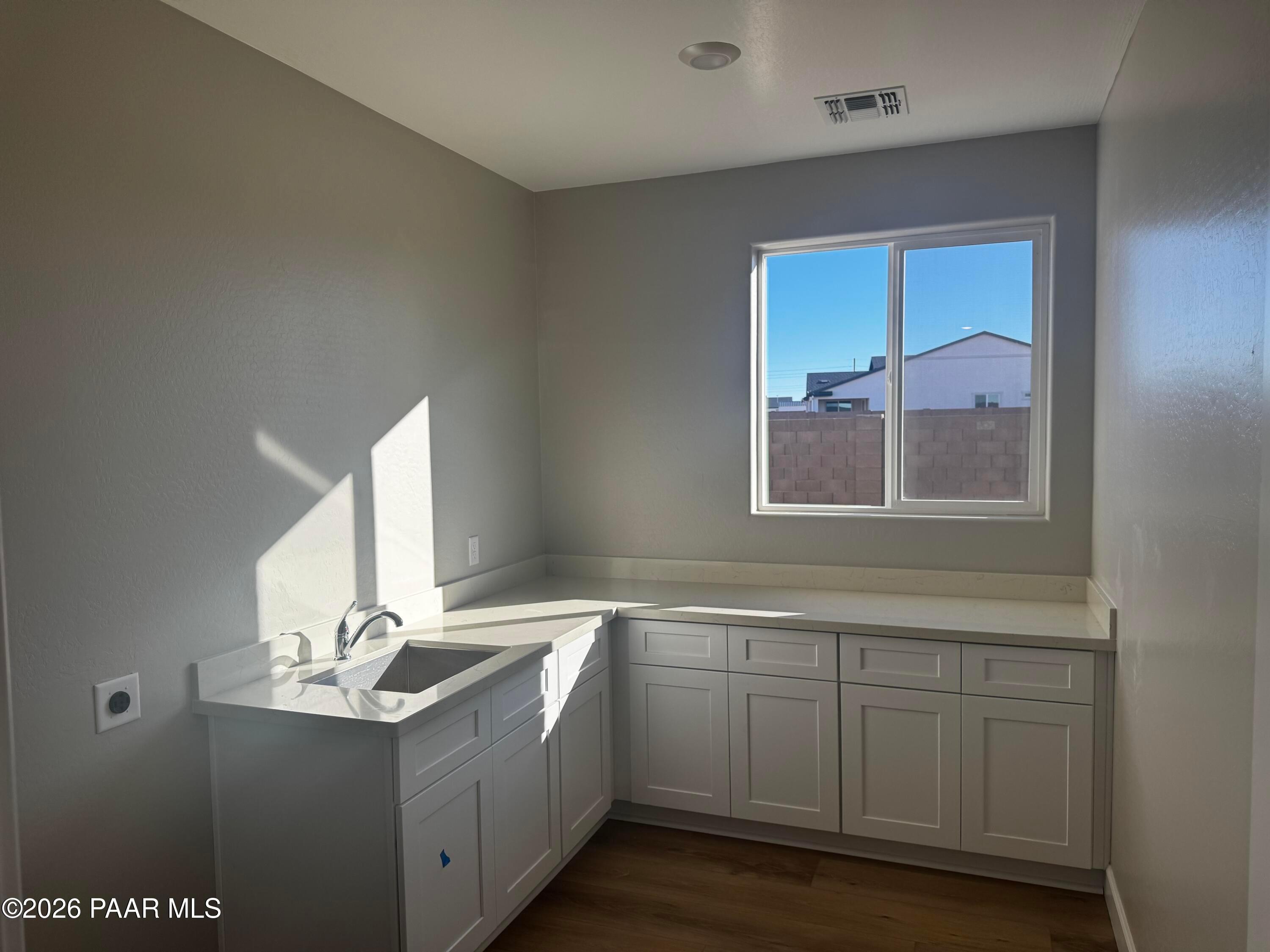 Bright laundry room with white shaker cabinets, corner sink, quartz counters, and large window in Evermore Homes The Monarch B, Prescott Valley