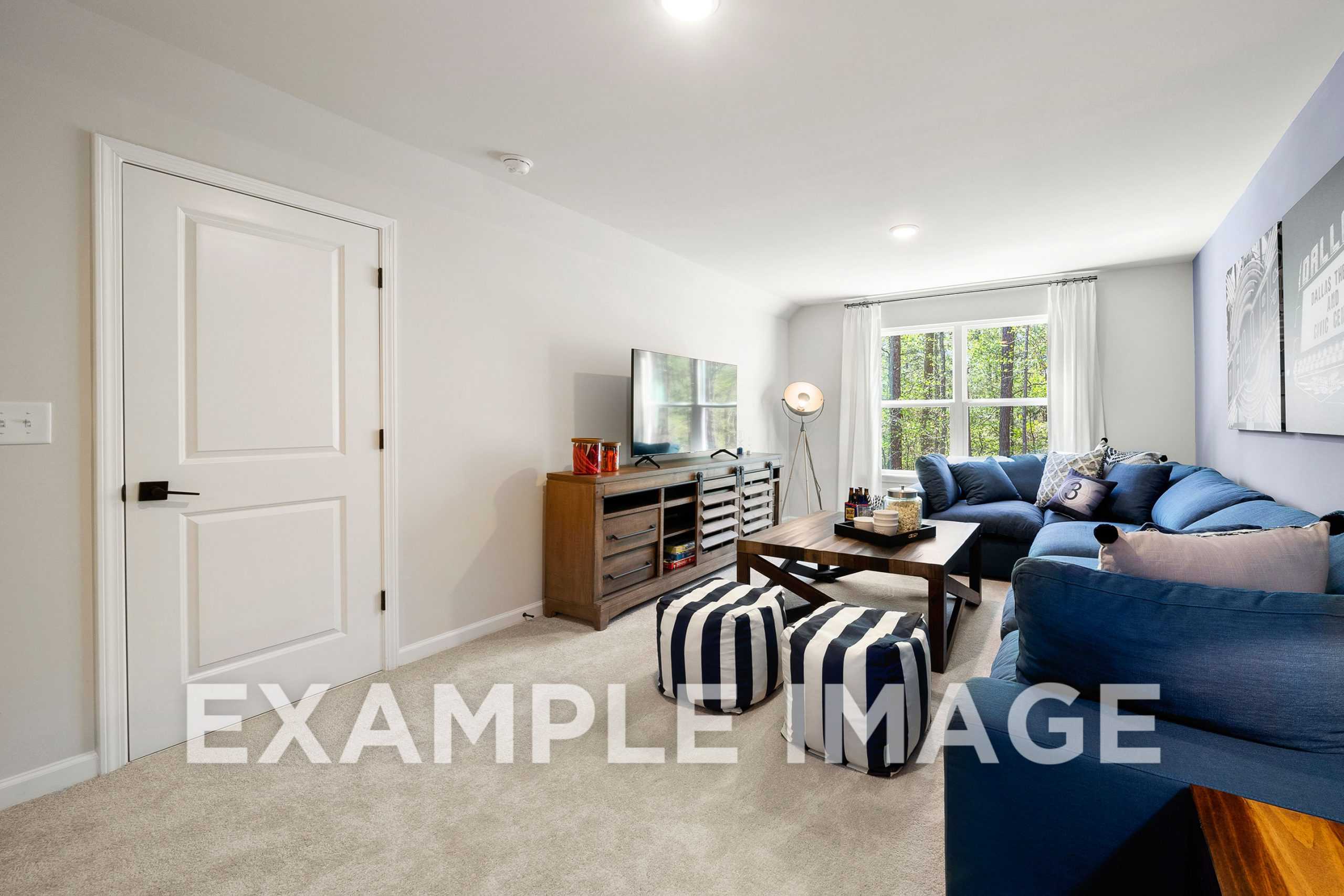 Cozy bonus room in The Hickory A home with navy blue sectional sofa, wooden TV console, striped poufs, and large window overlooking trees
