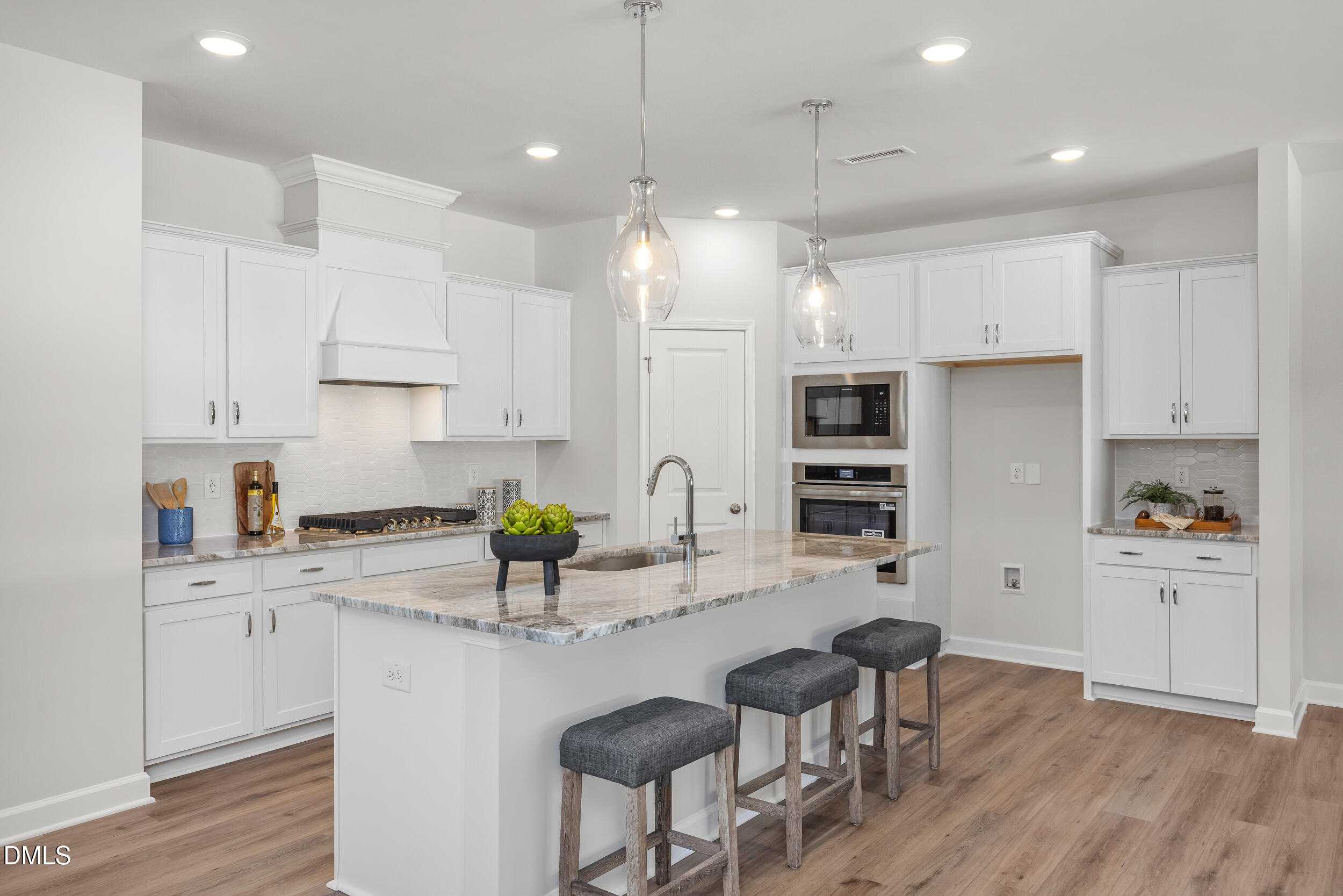 Modern white kitchen with large island, stainless double ovens, granite counters, and pendant lights in Davidson Homes Preston C, Lillington NC