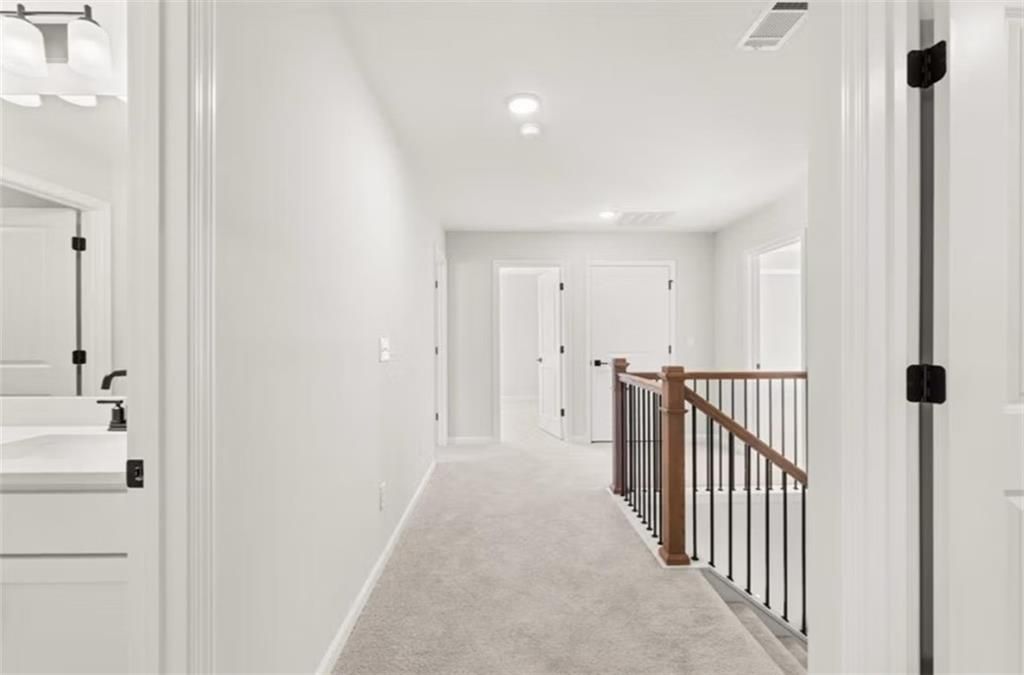 Bright upstairs hallway with carpeted floors, white walls, bedroom doors, and wooden staircase railing in Davidson Homes The Hickory B, Winder, Georgia