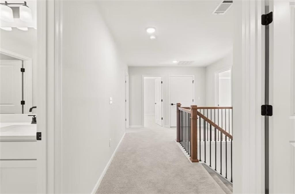 Bright upstairs hallway with carpeted floors, white walls, bedroom doors, and wooden staircase railing in Davidson Homes The Hickory B, Winder, Georgia