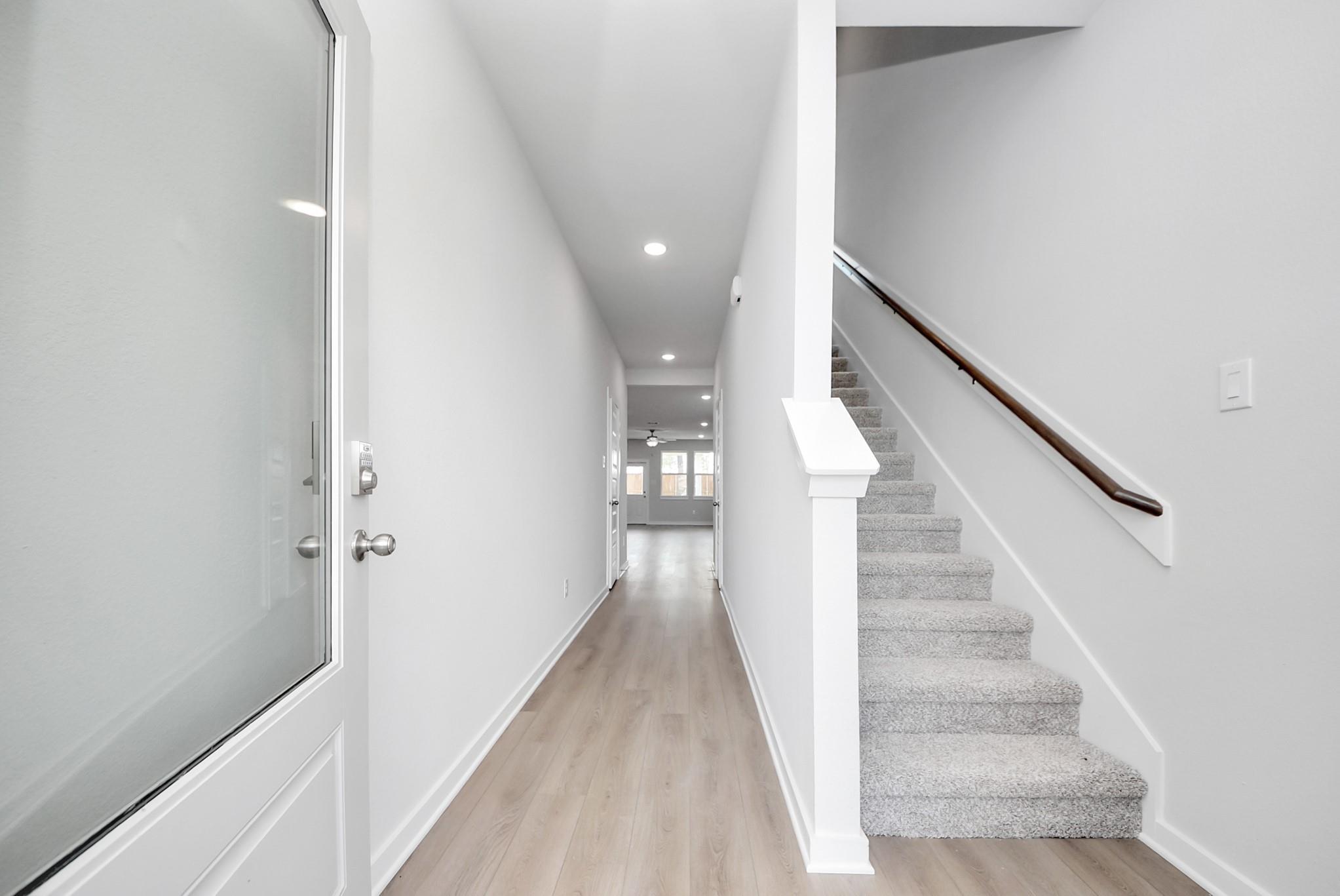 Bright entryway with luxury vinyl plank flooring and carpeted staircase in The Blanco F floor plan, Spring Branch Crossing.