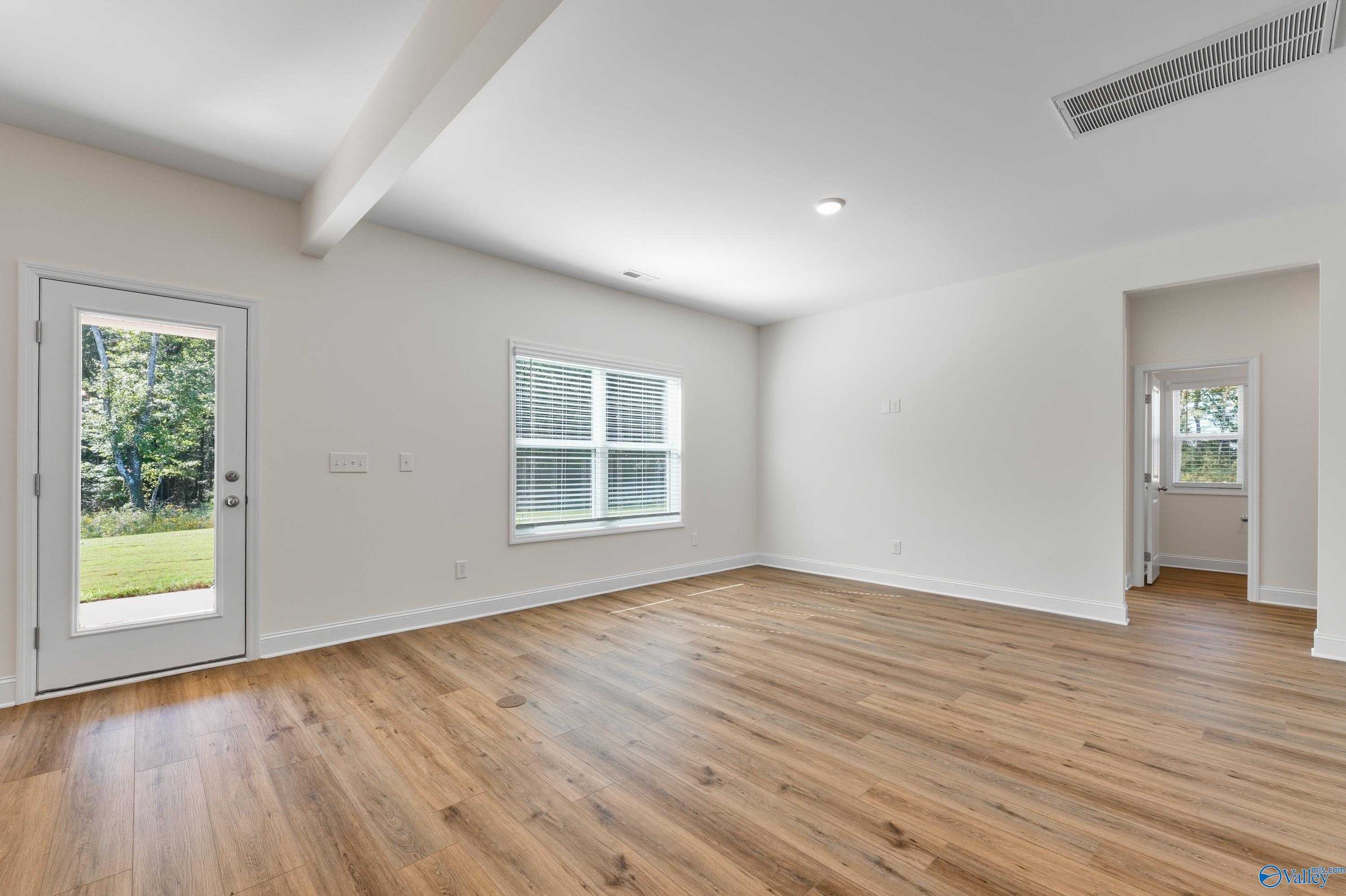 Bright family room with hardwood floors, beige walls, and glass door to lush backyard in Davidson Homes The Shelby A, Athens AL