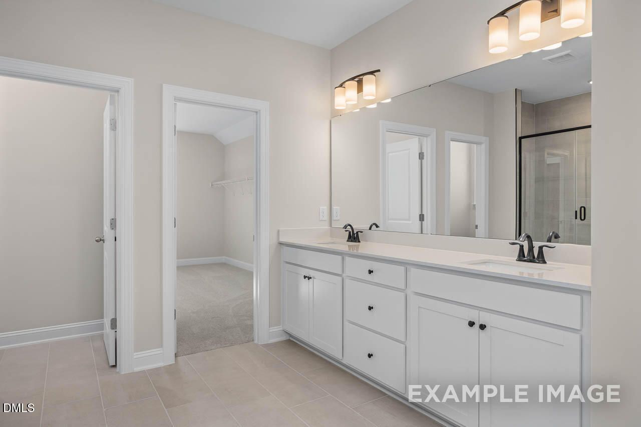 Elegant master bathroom with white double vanity, quartz counters, mirrors, and glass shower in Davidson Homes Crawford D, Angier, NC