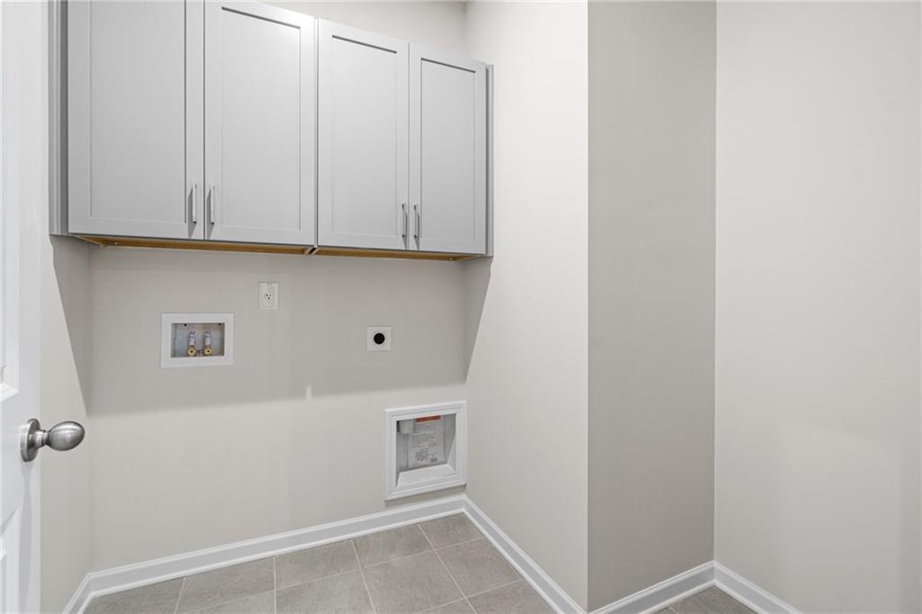 Laundry room with grey cabinets and tile flooring in The Glenwood A floor plan at Wehunt Meadows in Hoschton, Georgia.