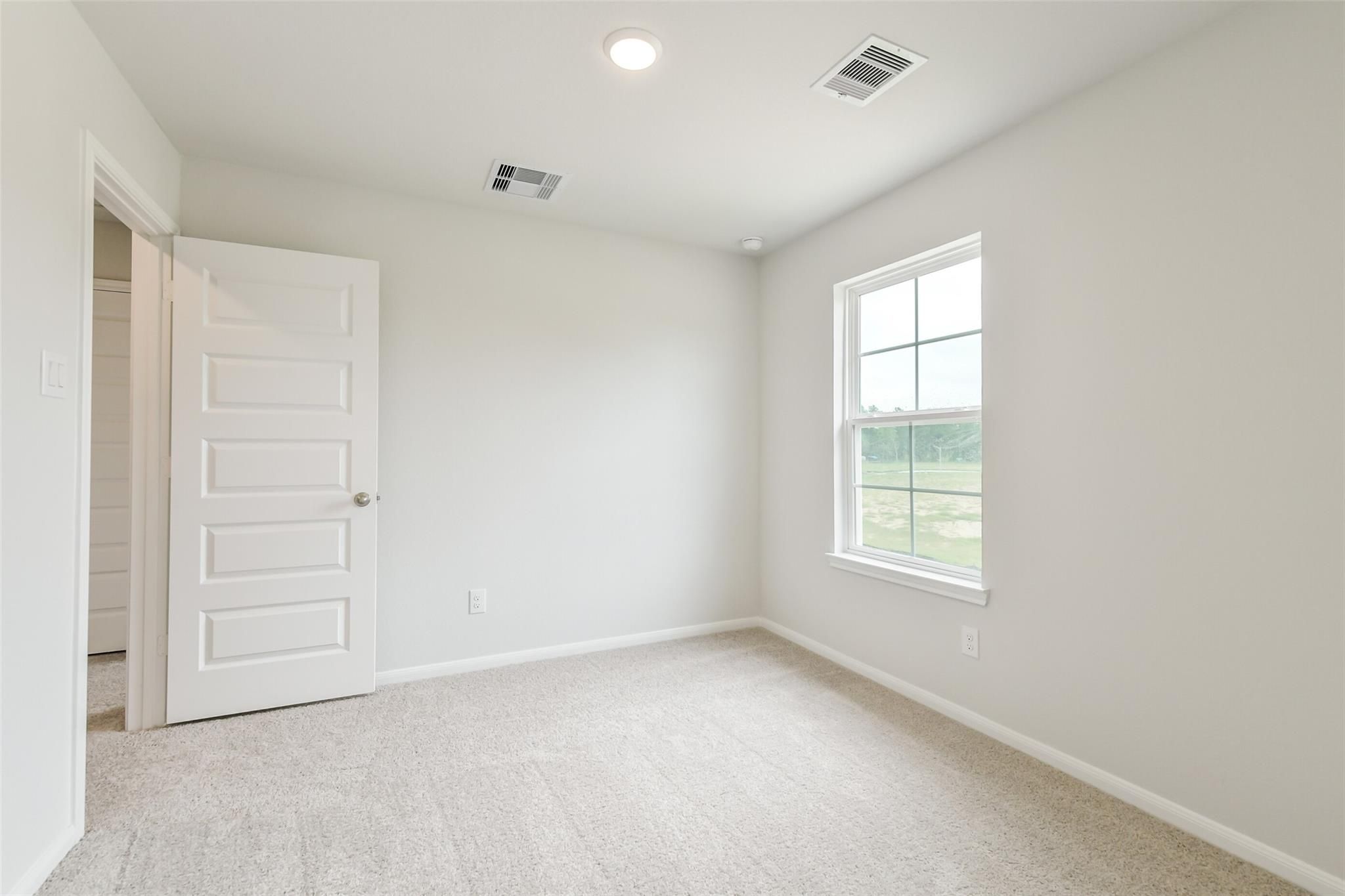 Bright bedroom with beige carpet, large window to green fields, and adjacent bath door in Davidson Homes The Brazos F, Conroe TX
