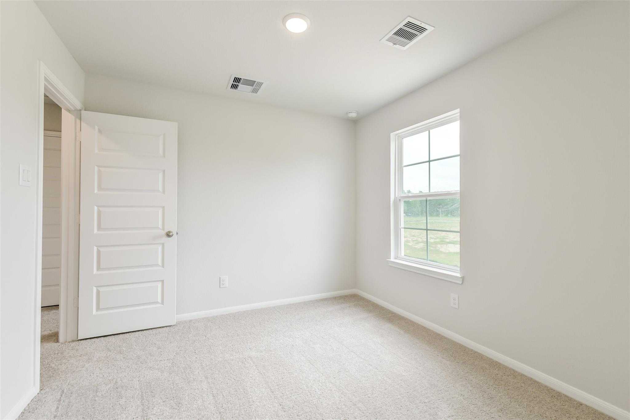 Bright bedroom with beige carpet, large window to green fields, and adjacent bath door in Davidson Homes The Brazos F, Conroe TX