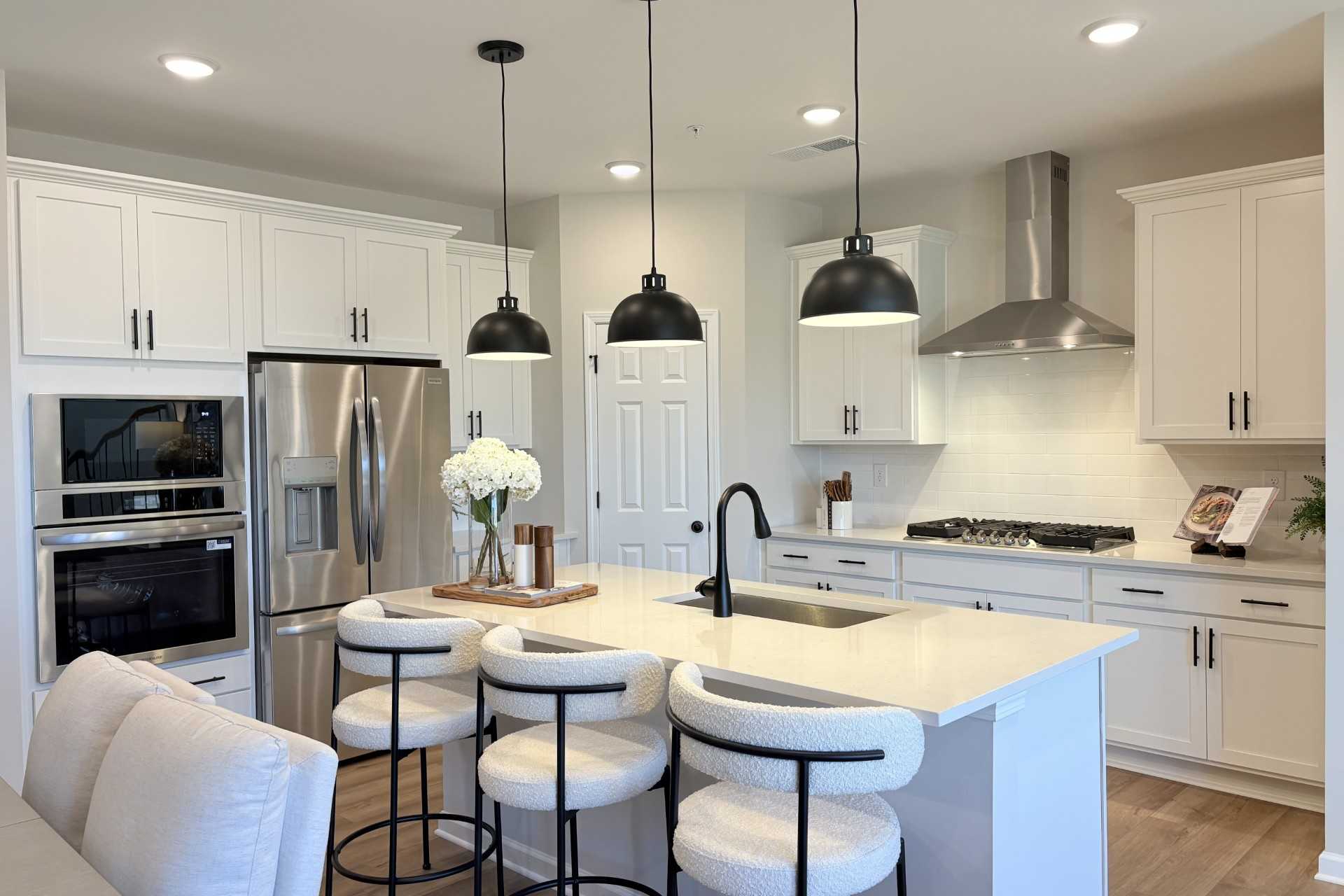 Modern white kitchen with central island, bar stools, stainless appliances, and pendant lights at Hemingway in Cumming GA