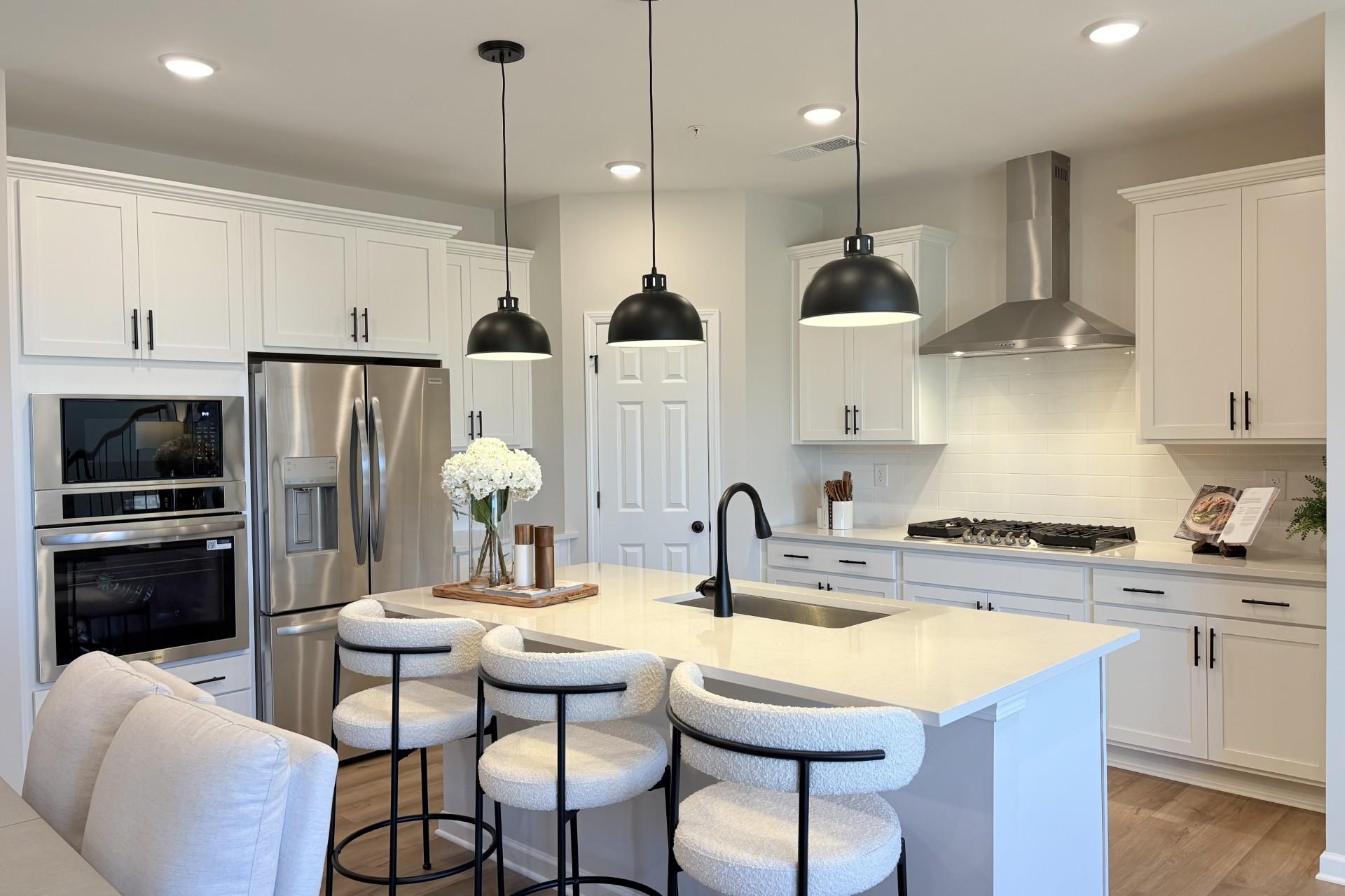 Modern white kitchen with central island, bar stools, stainless appliances, and pendant lights at Hemingway in Cumming GA