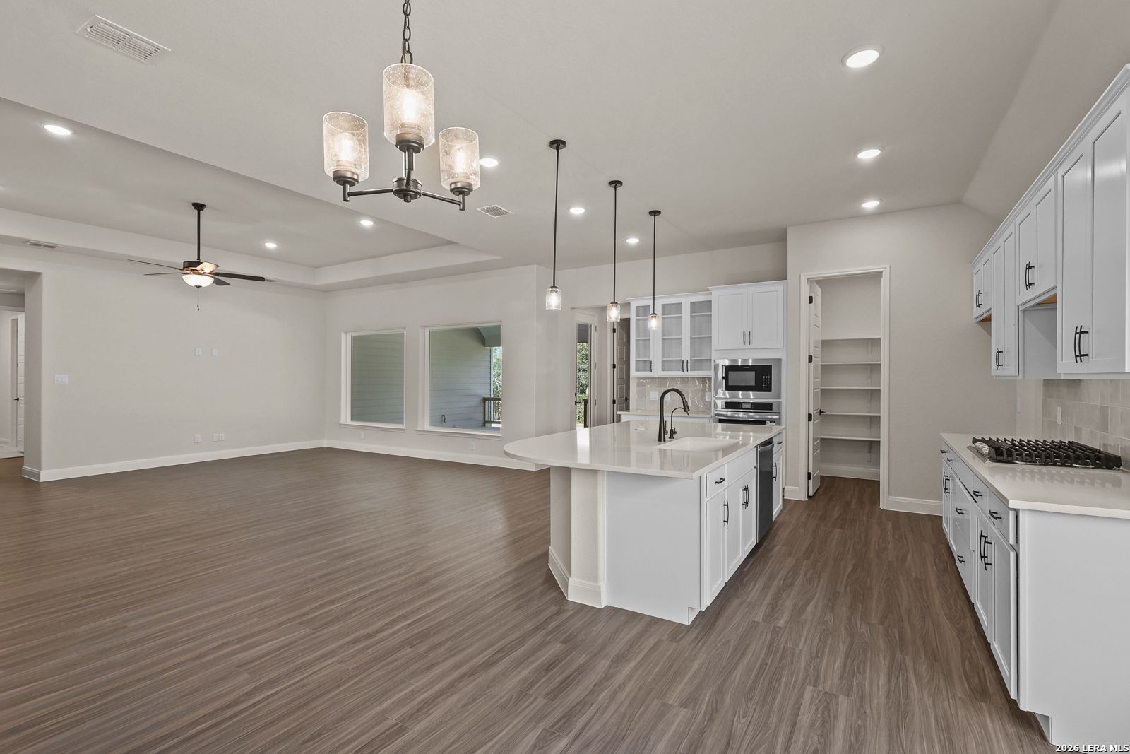 Open-concept kitchen with white cabinets and quartz island in The Summerlin B floor plan at Potranco Oaks, Castroville, TX.