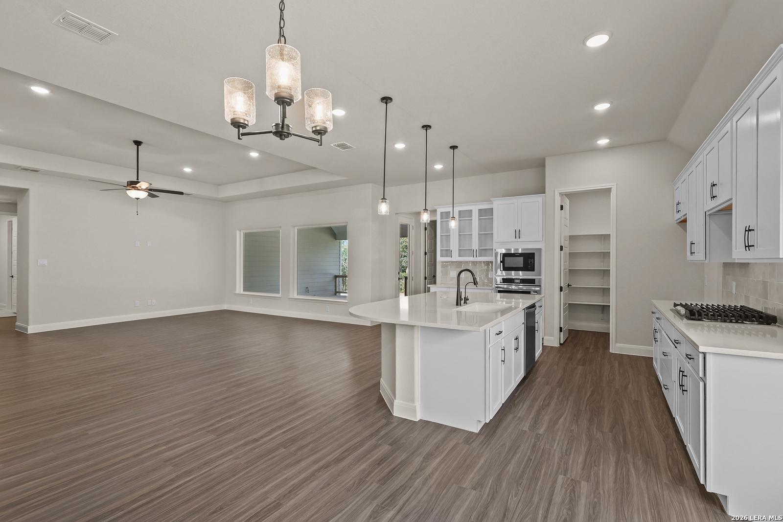 Open-concept kitchen with white cabinets and quartz island in The Summerlin B floor plan at Potranco Oaks, Castroville, TX.
