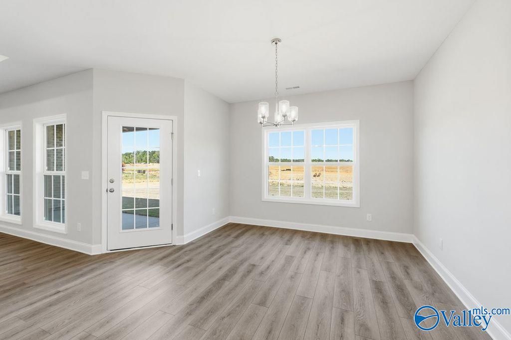 Bright dining area with light gray walls, luxury vinyl plank floors, modern chandelier, and large windows overlooking pasture in The Harrison home, Hartselle, AL